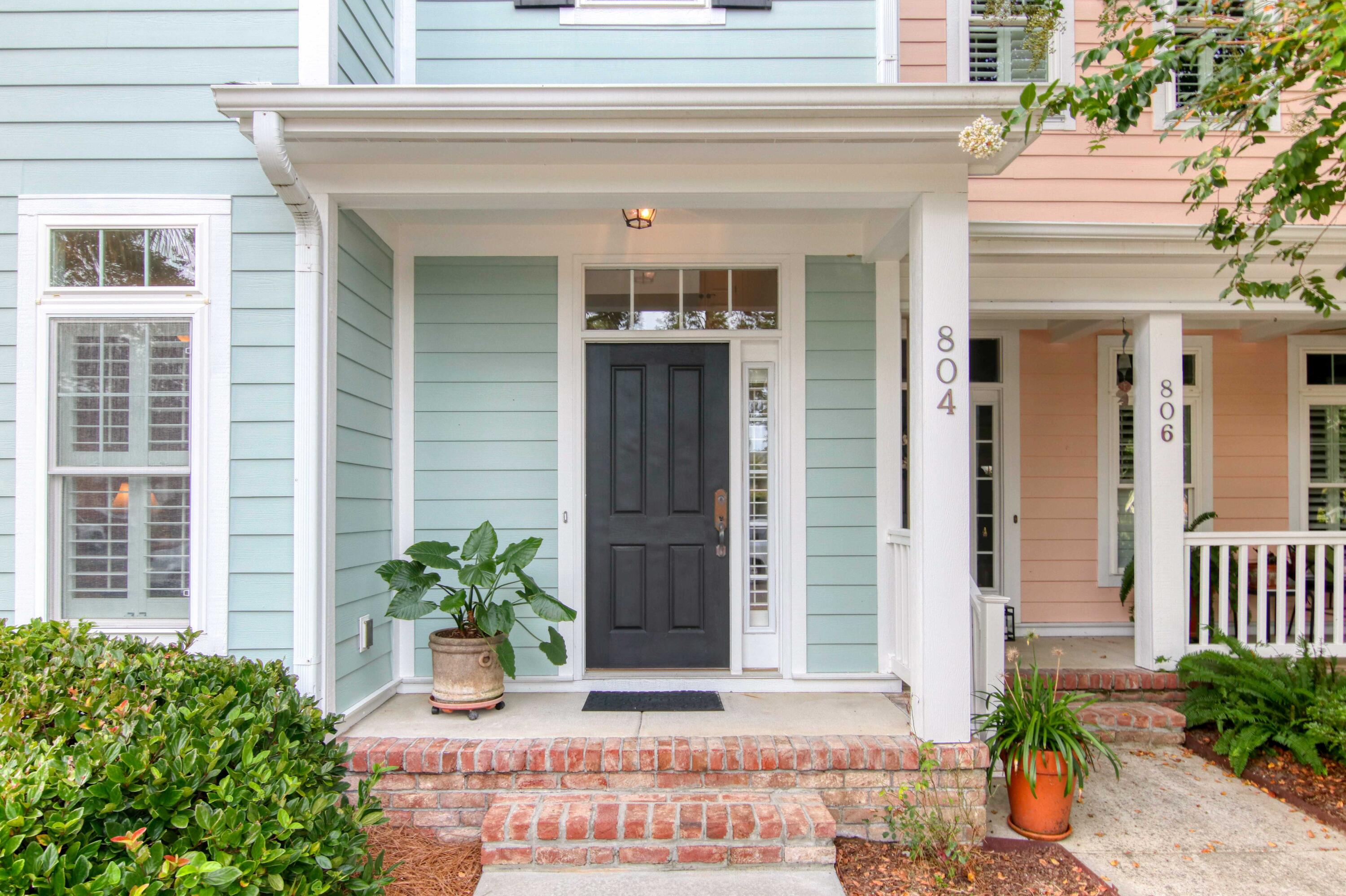 Front entrance with a dark paneled door, pale blue siding, white columns, and brick steps.