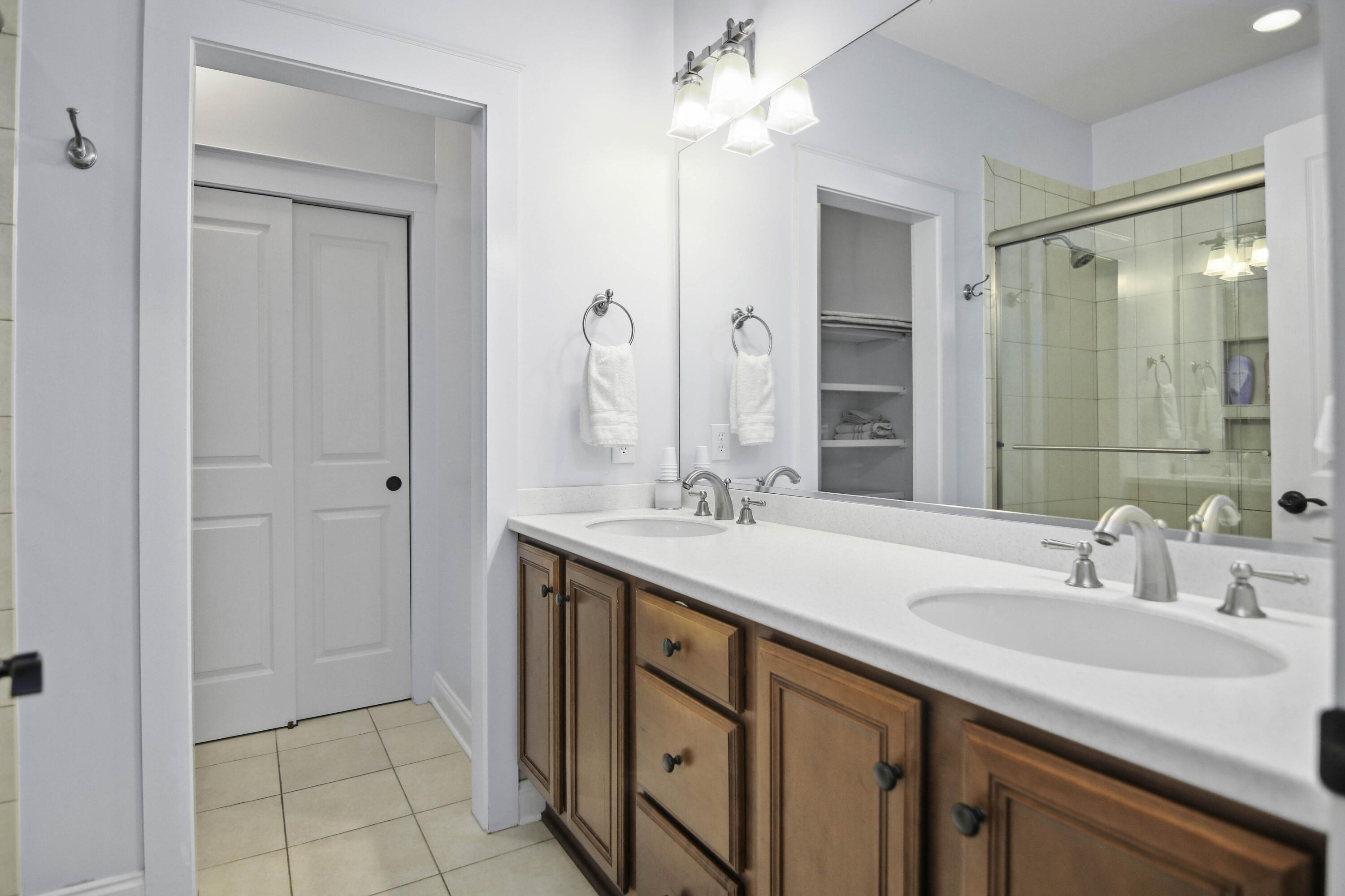 Bathroom with a double-sink vanity, warm wood cabinets, and a glass-enclosed tiled shower.