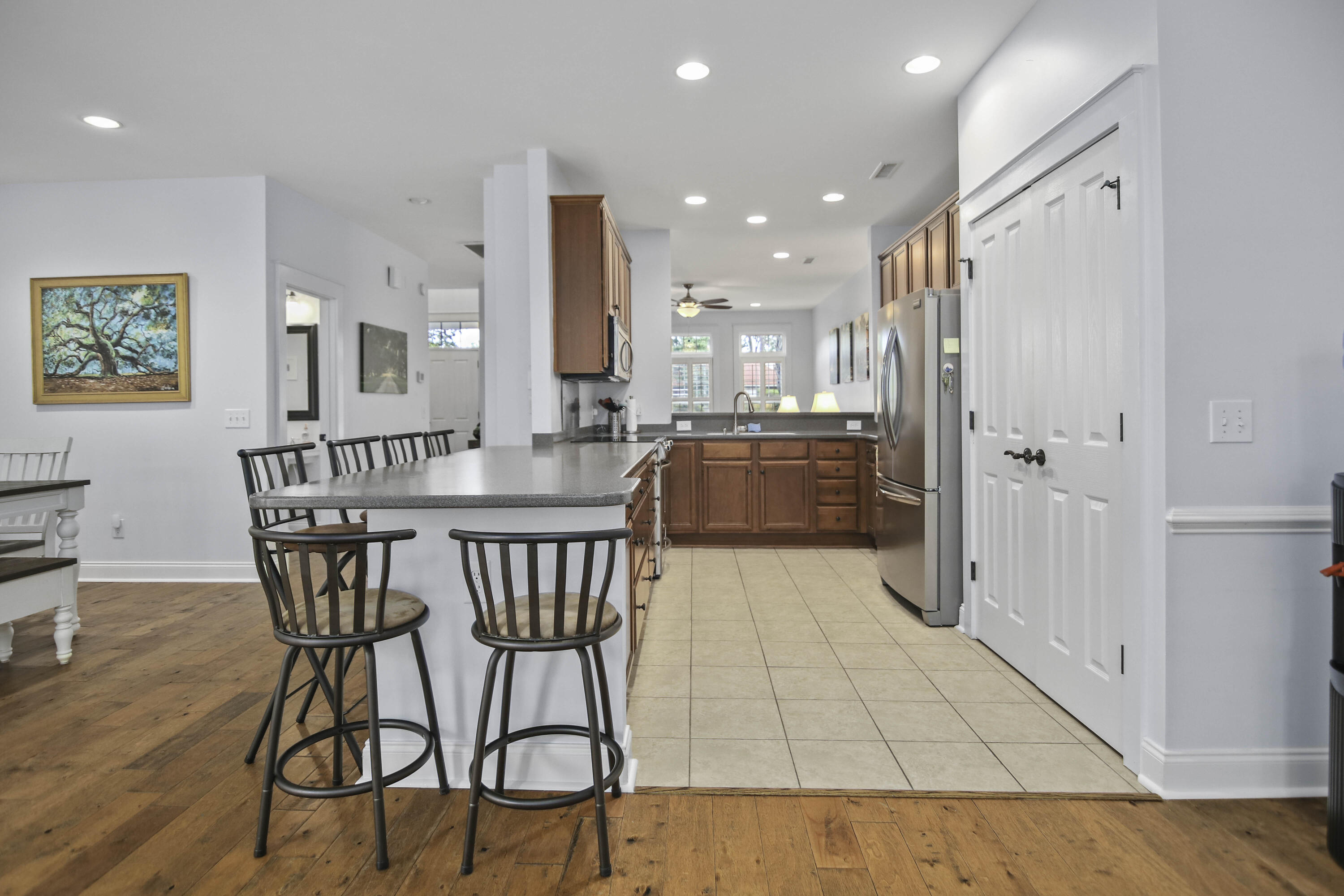 Open kitchen with reddish wood cabinets, stainless appliances, and a long breakfast bar with dark stools.
