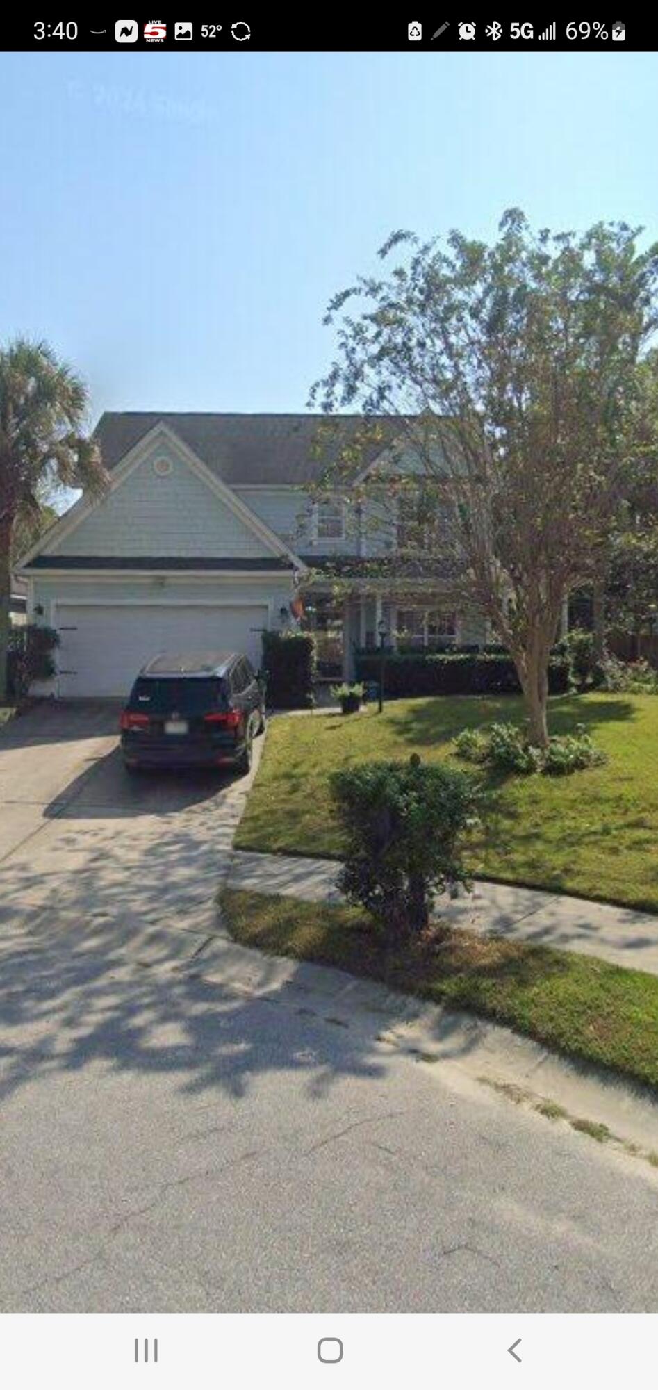 Two-story blue-gray house with a double garage, driveway, front lawn, and mature trees.