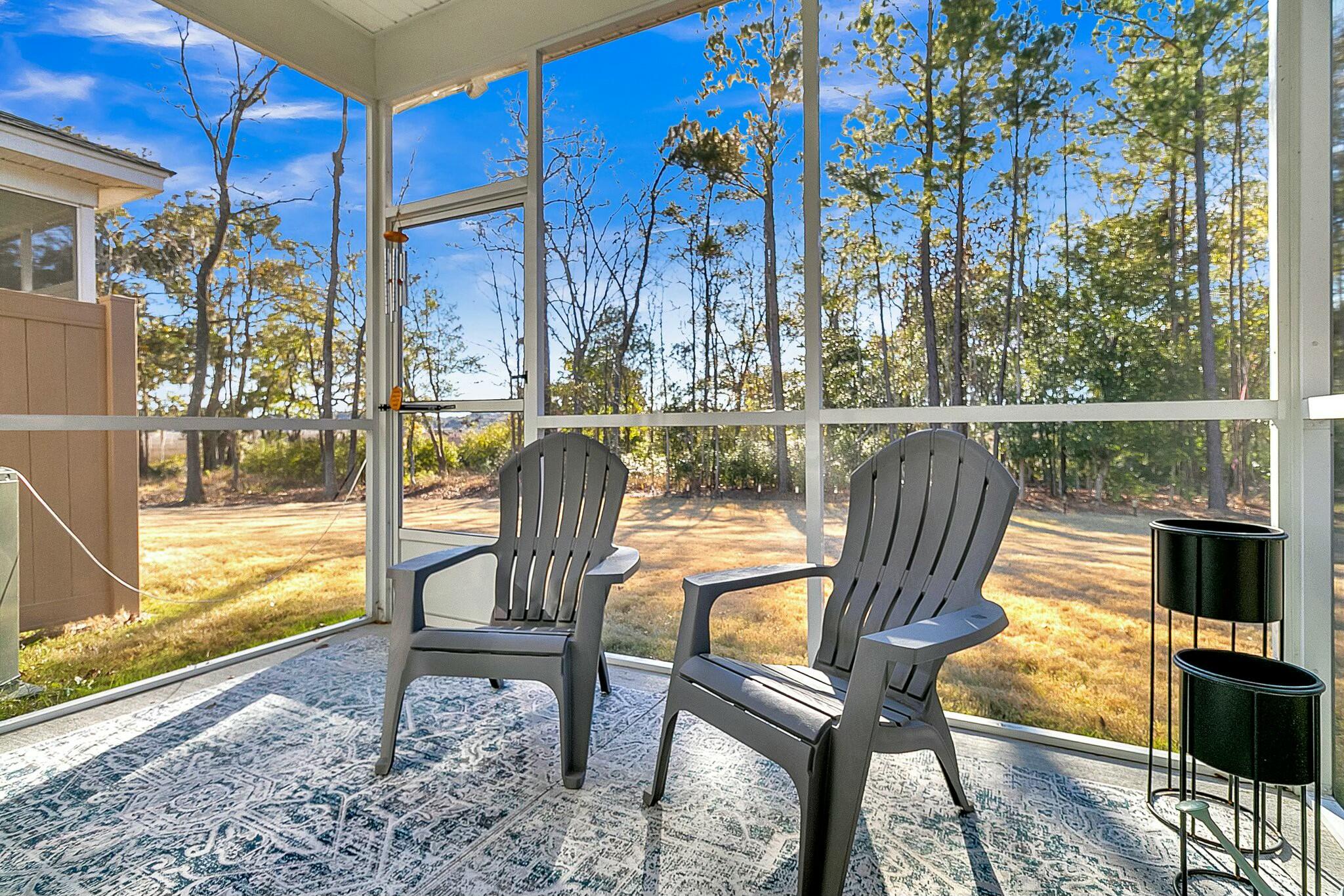 Screened porch with two Adirondack chairs and a sunny wooded backyard view.