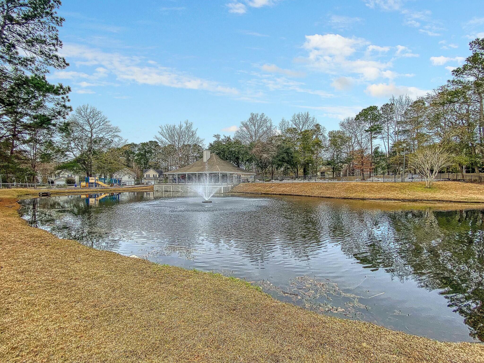 Community pond with a fountain, pavilion, and playground along the far bank.