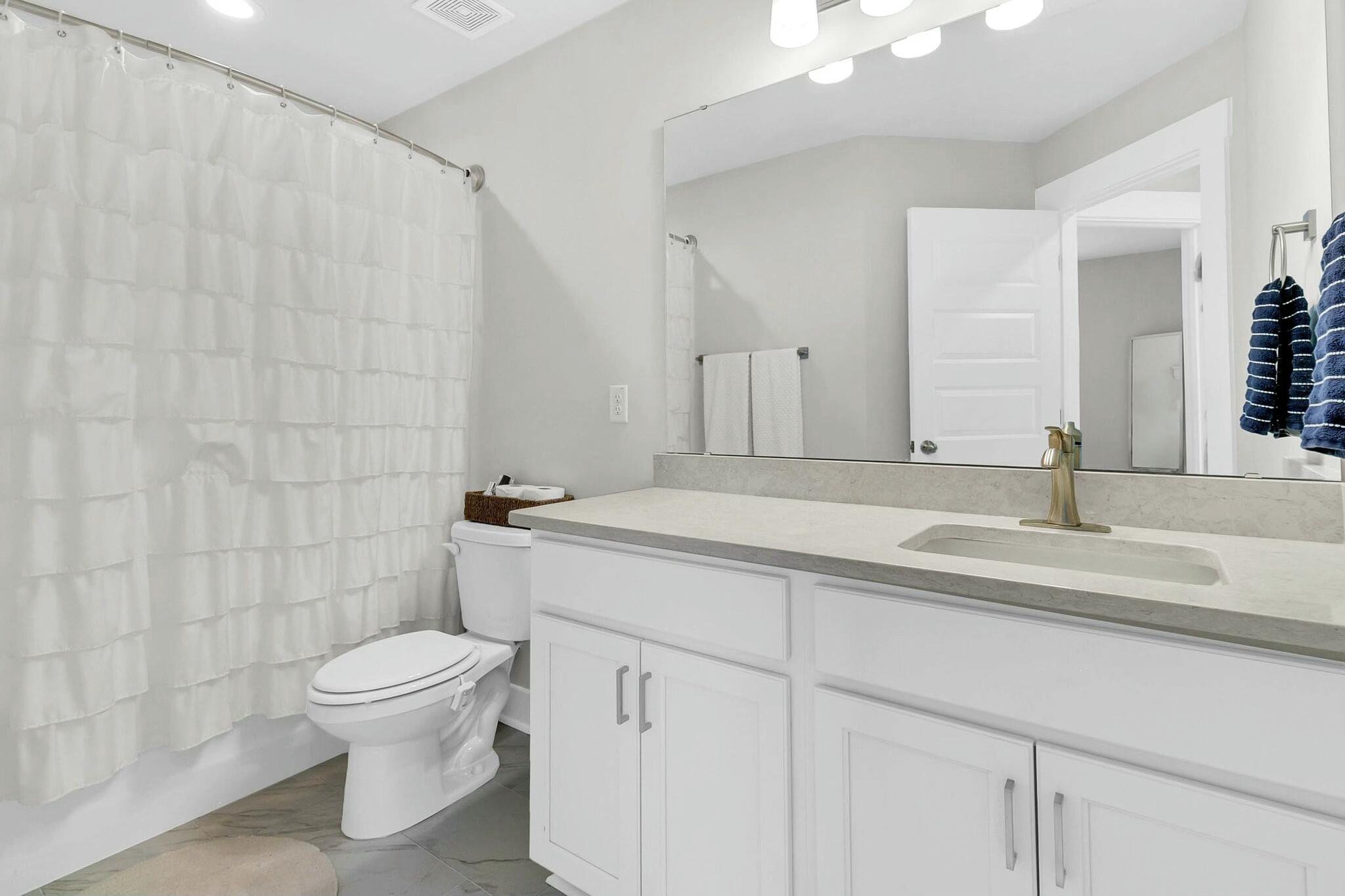 Bathroom with a white vanity, brass faucet, large mirror, and ruffled shower curtain.