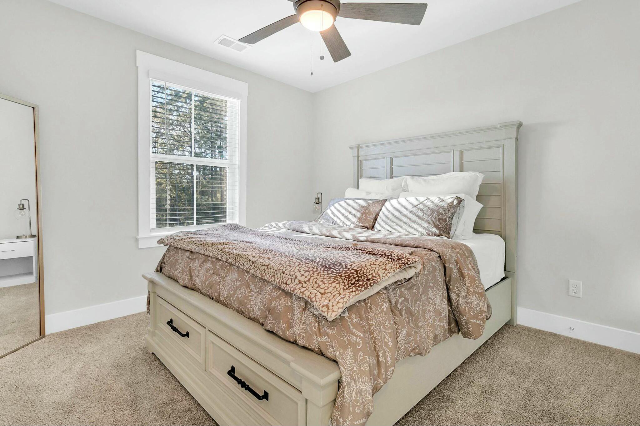 Furnished bedroom with a cream bed, patterned taupe bedding, a bright window, and a ceiling fan.