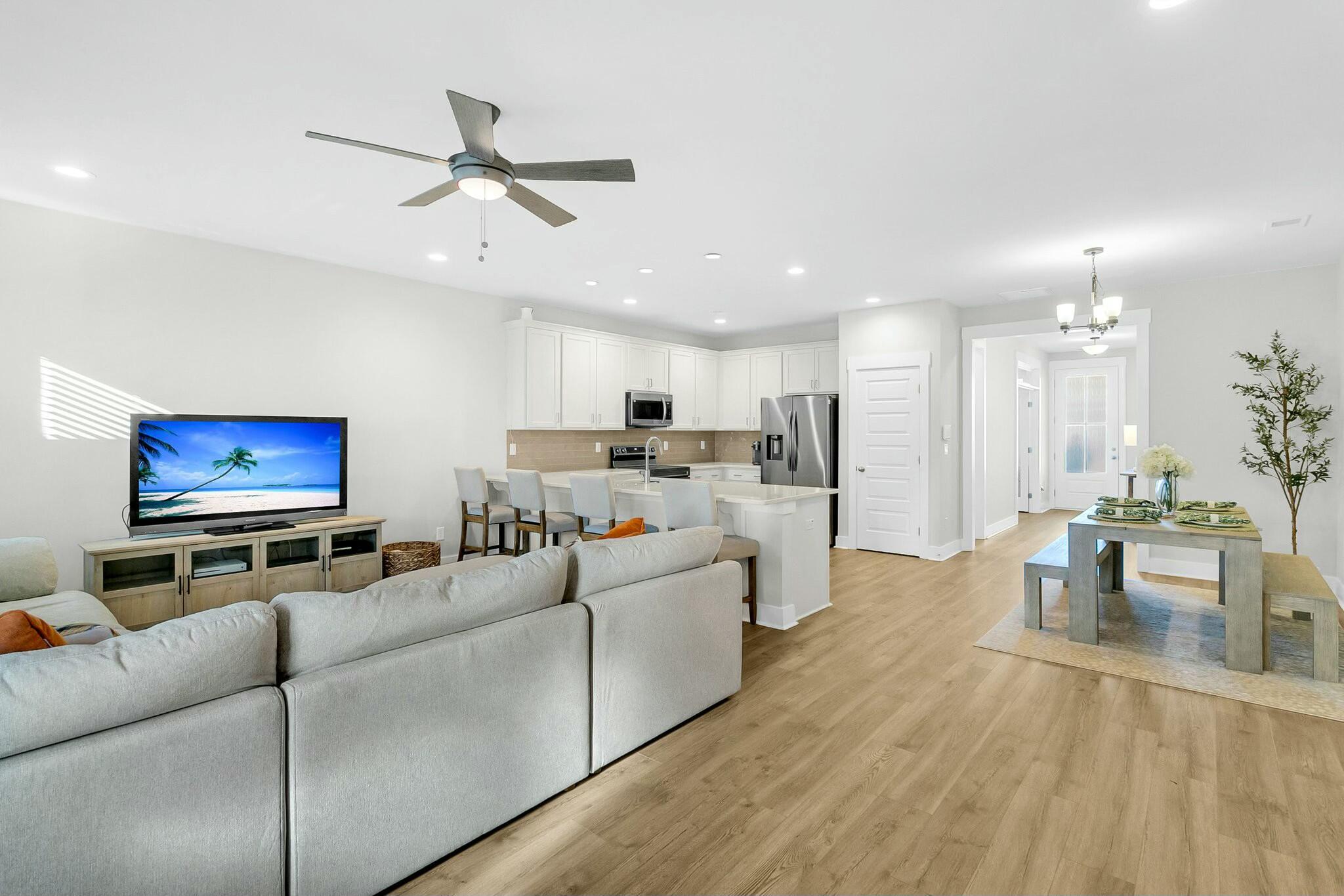 Open-plan living room with gray sectional, kitchen island, and white kitchen cabinetry.