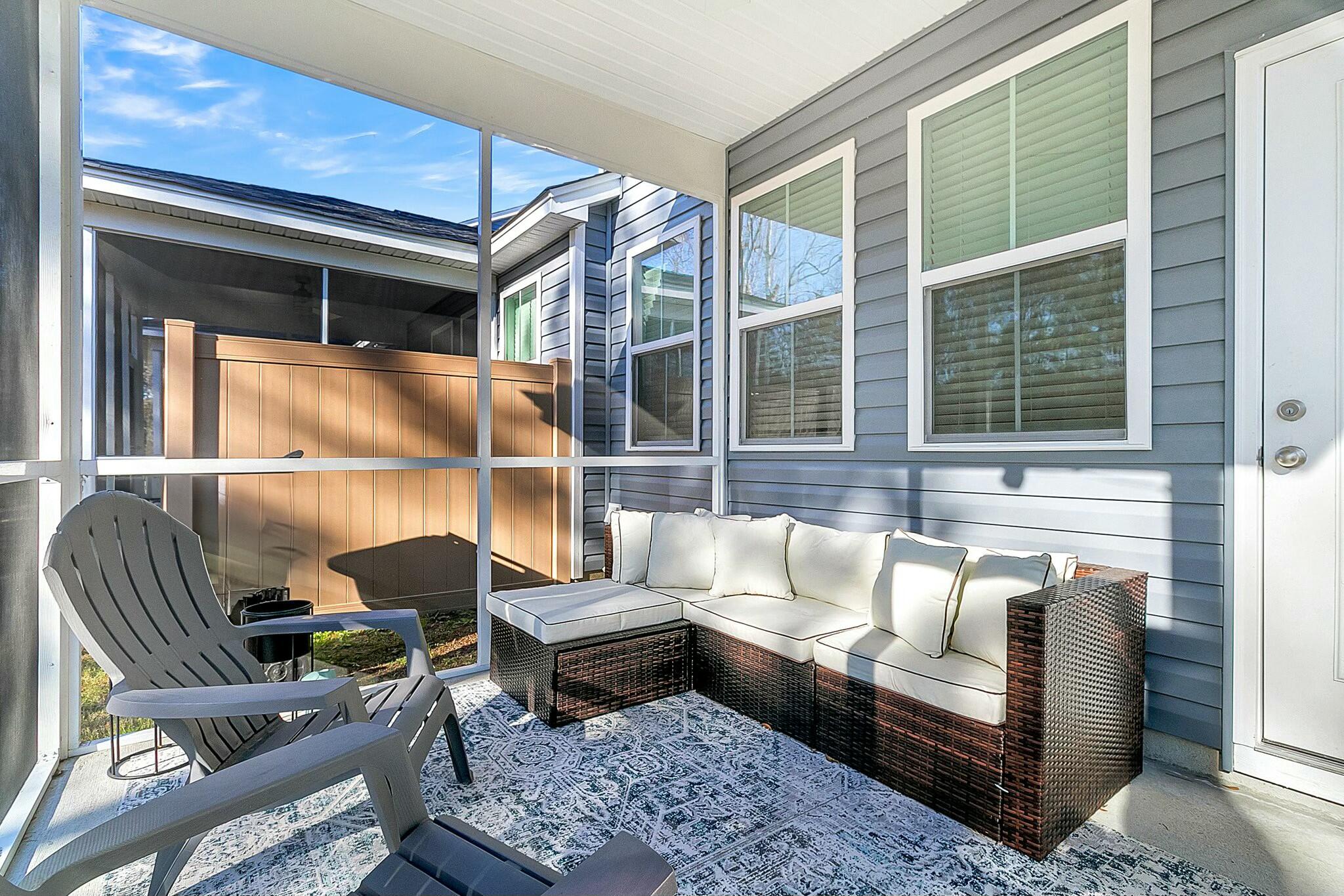 Screened porch with a white wicker sectional, Adirondack chairs, and a view of the fenced yard.