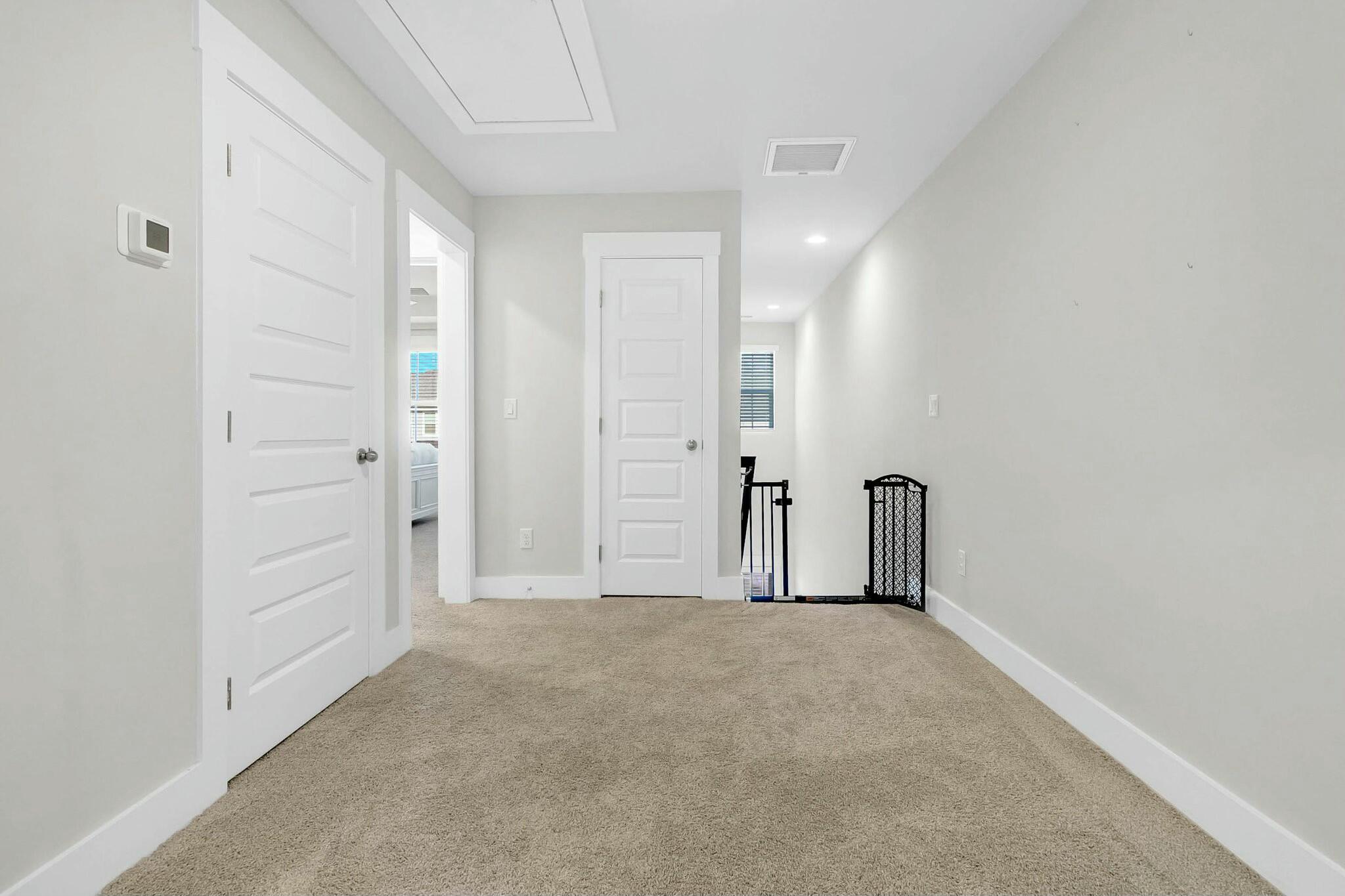 Empty carpeted hallway with white paneled doors and a safety gate at the stair opening.