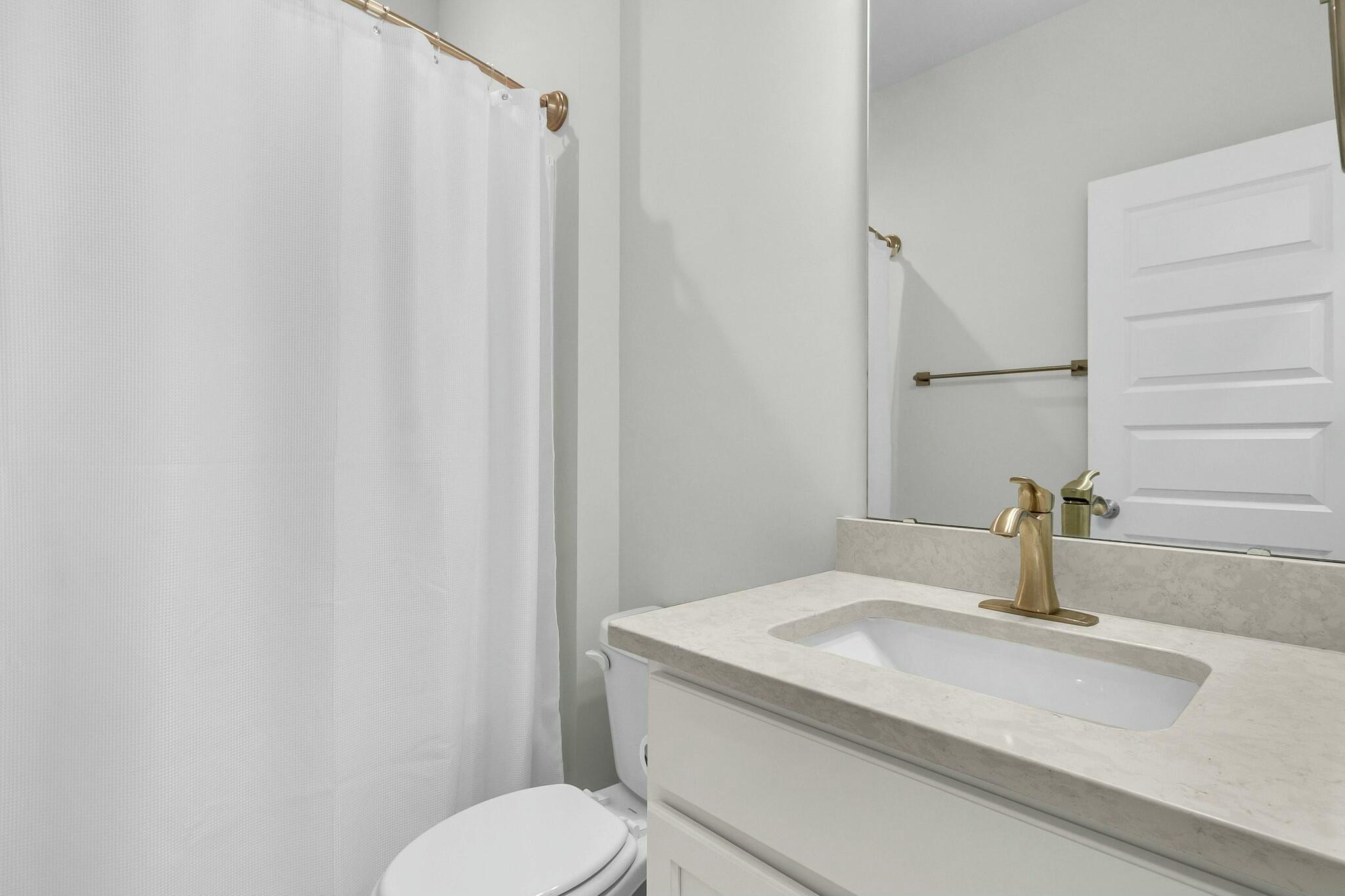 Bathroom with a white shower curtain, stone vanity countertop, and brushed brass faucet.