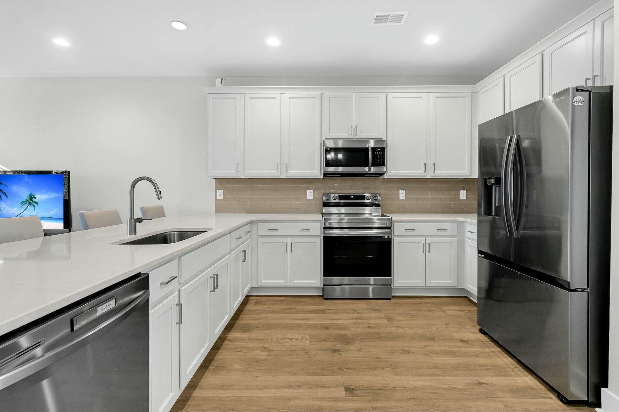 Modern kitchen with white cabinetry, stainless steel appliances, a large island, and warm wood-look floors.