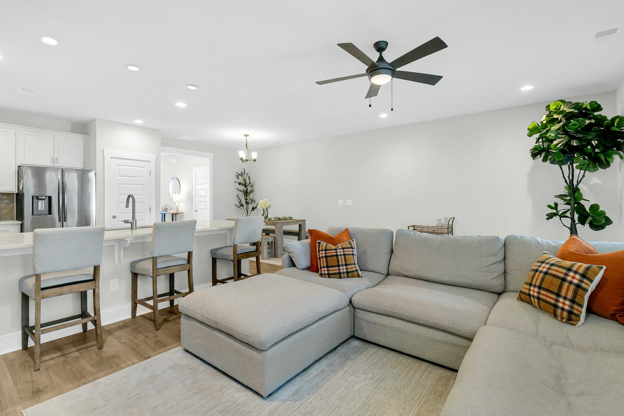 Open-plan living room with a gray sectional, plaid and orange pillows, and kitchen island with bar stools.