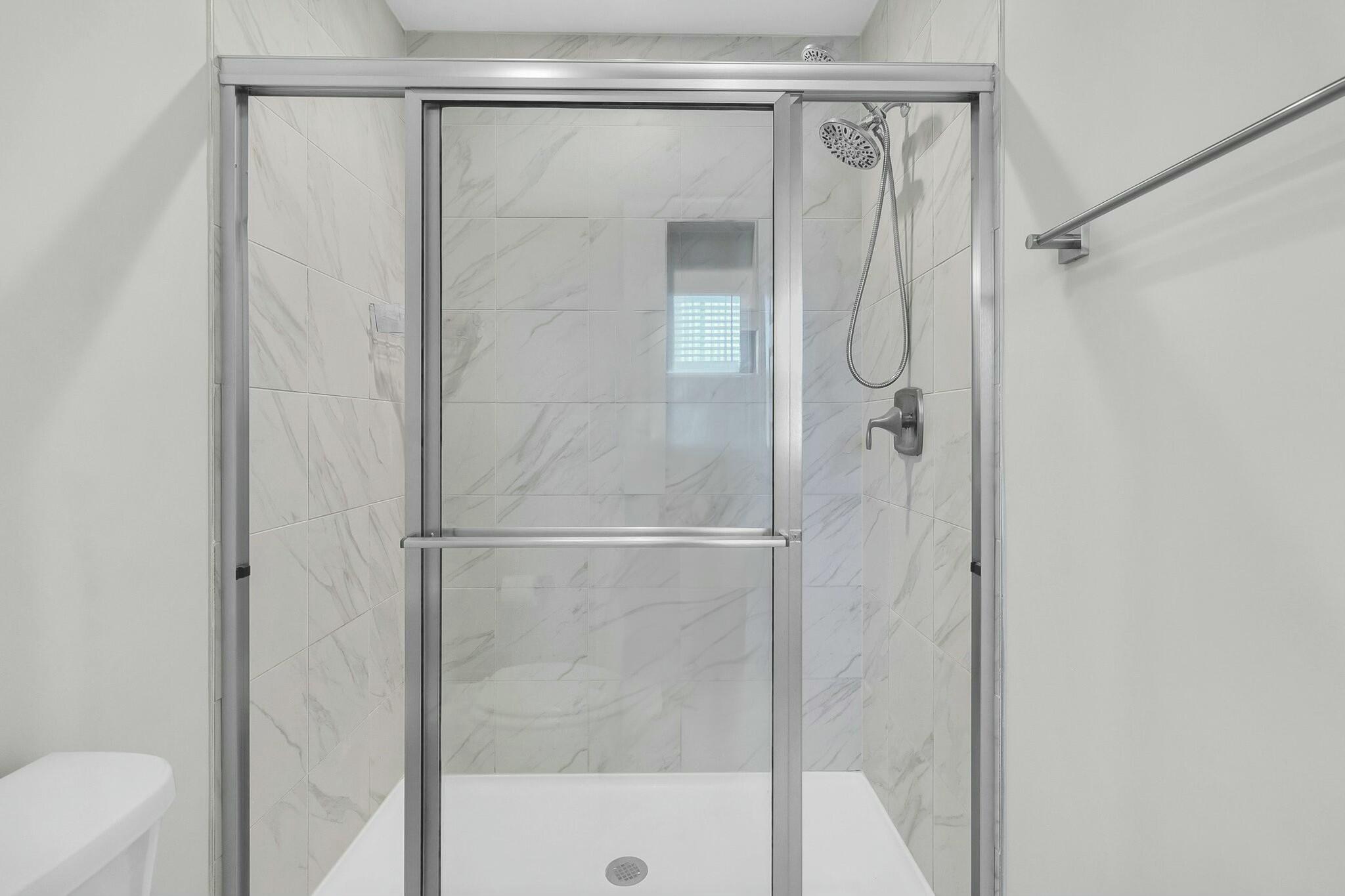 Bathroom shower with marble-look tile, glass enclosure, and handheld showerhead.