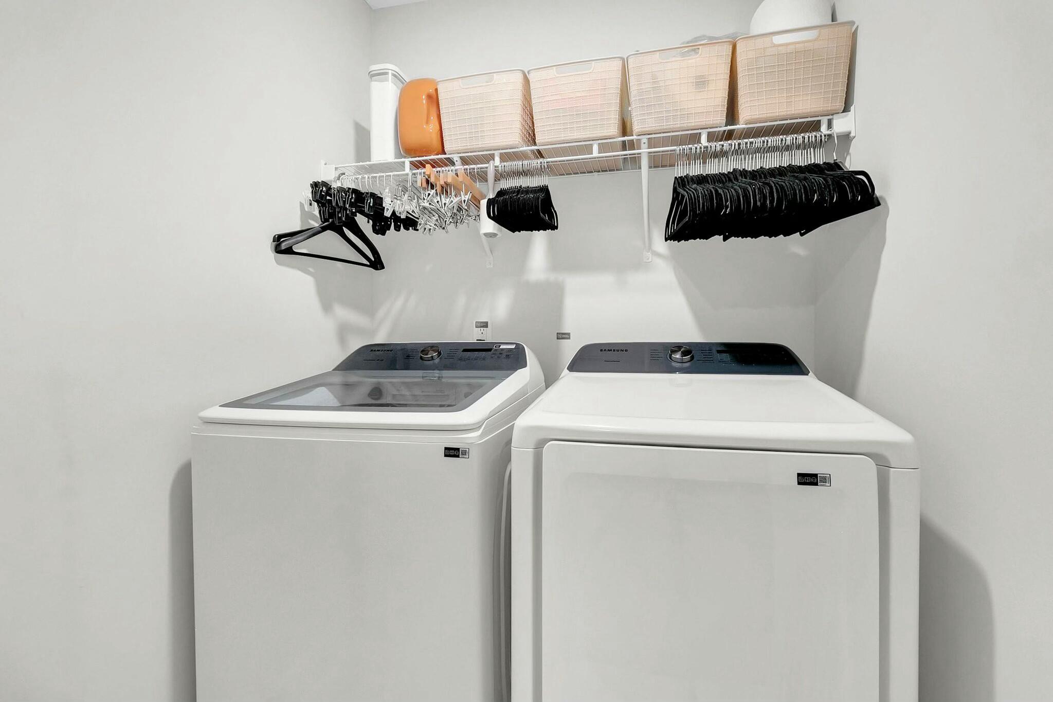 Laundry room with a washer and dryer beneath a shelf of baskets and hangers.