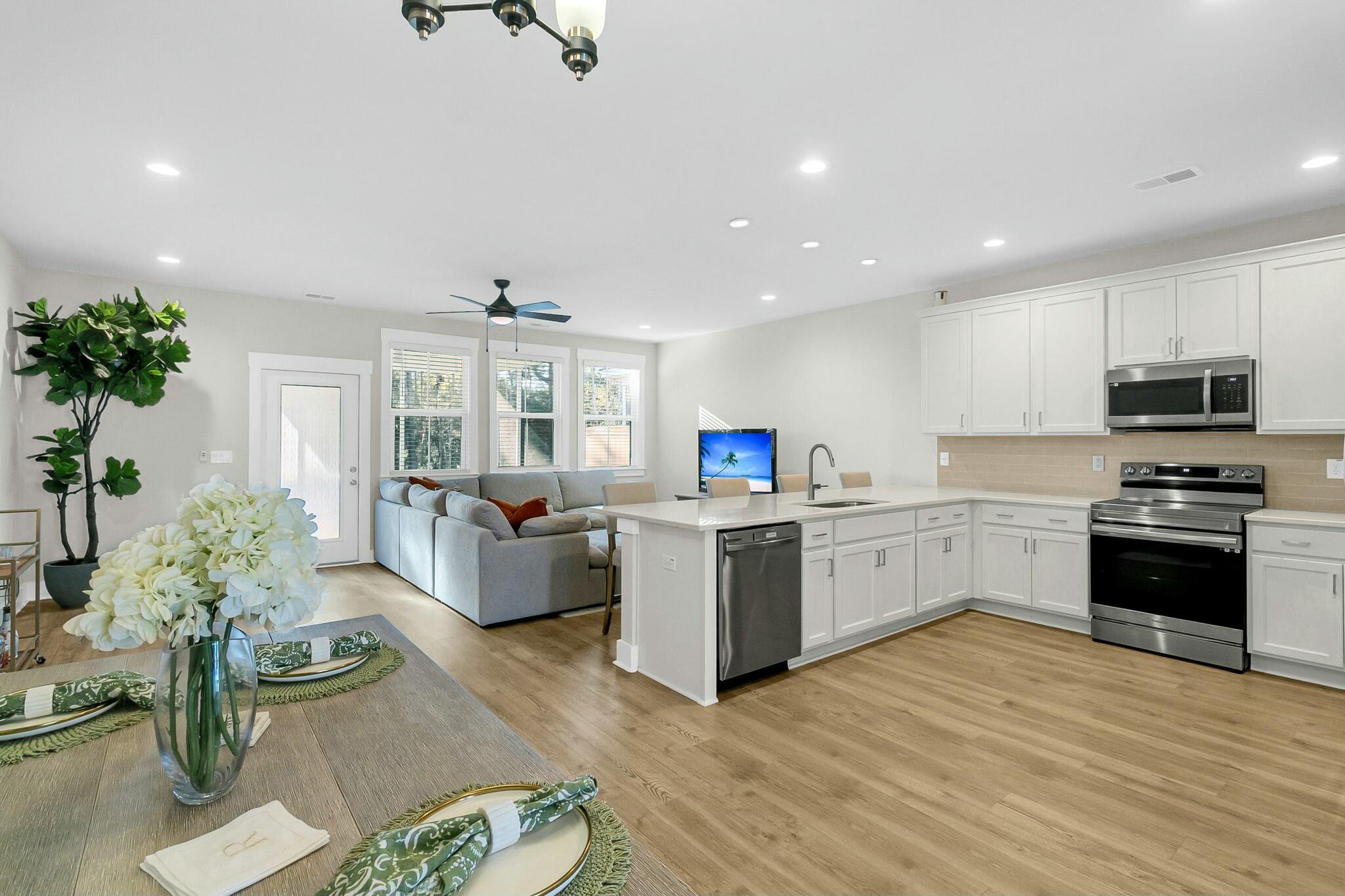 Open-plan kitchen and living room with a white island, stainless appliances, and gray sofa by three windows.