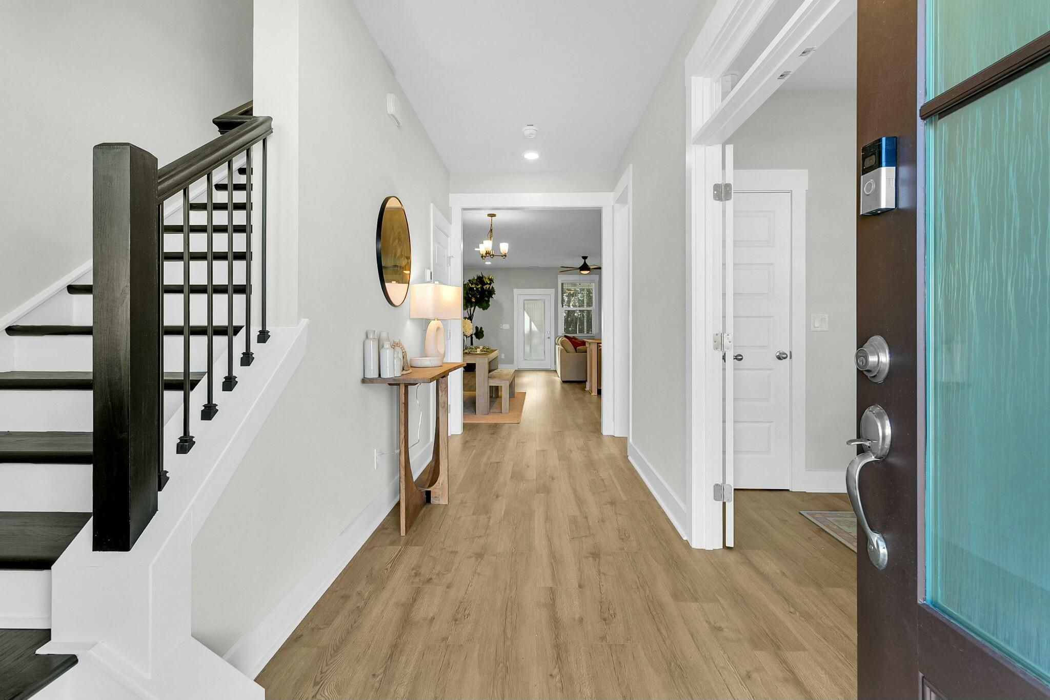Entry hall with wood floors, a dark-railed staircase, and an open glass-paneled front door.
