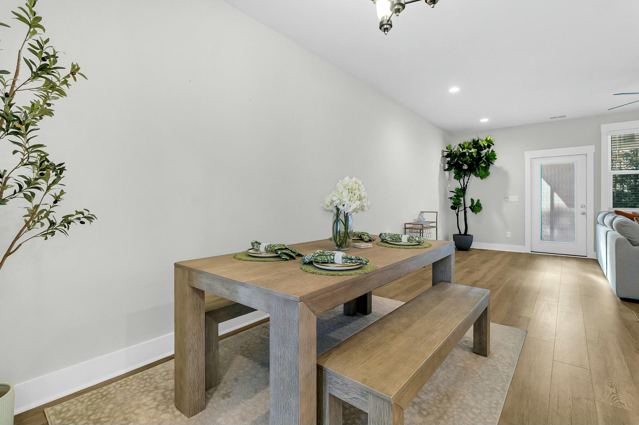 Staged dining room with a wood table set for four, white flowers, and a matching bench.