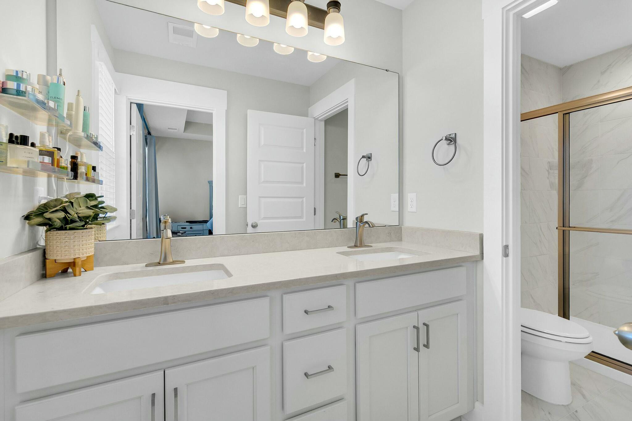 Bathroom with a double-sink vanity, large mirror, and tiled tub-shower with gold-tone trim.