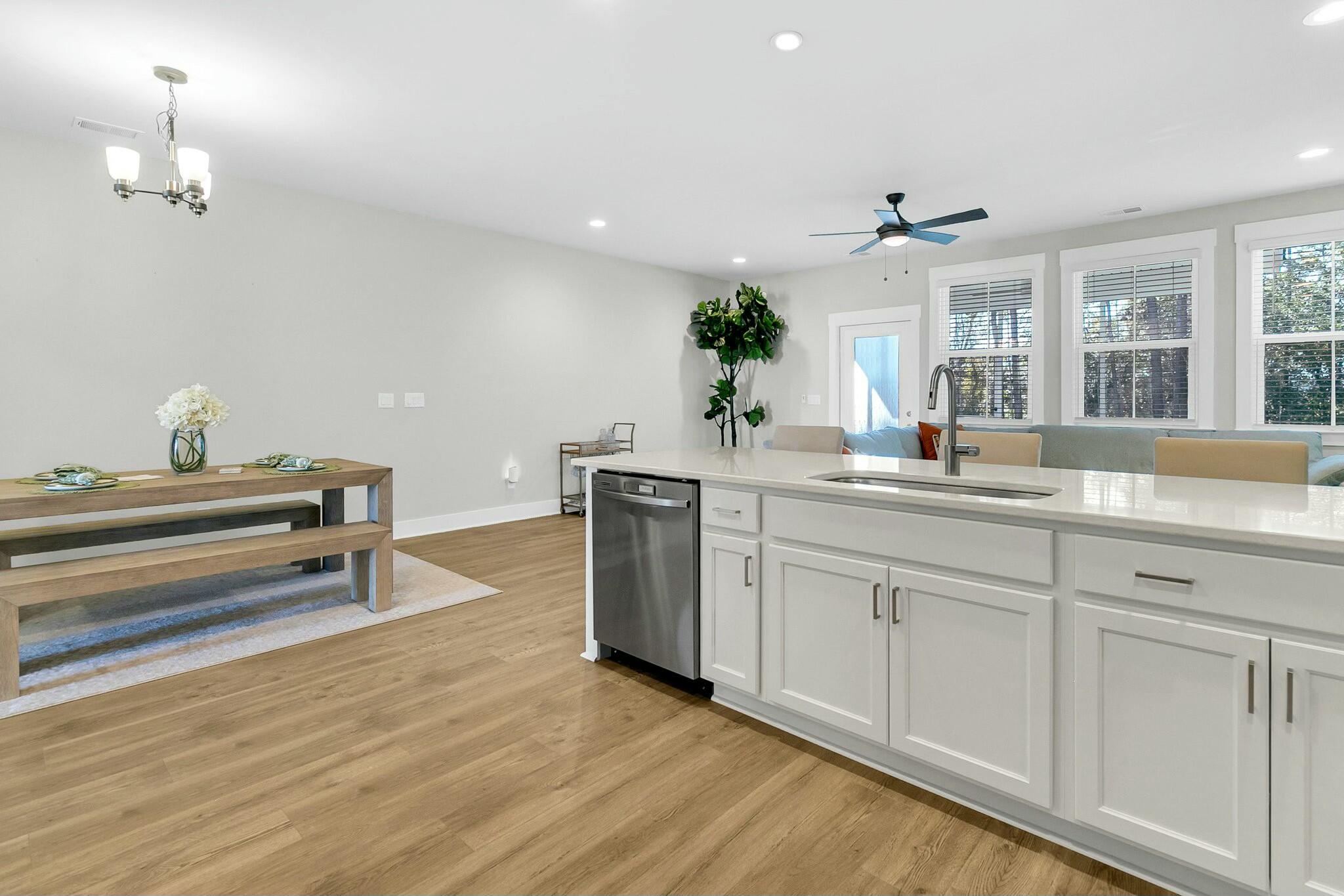 Open-plan kitchen with a long white island, stainless steel dishwasher, and adjoining dining table.