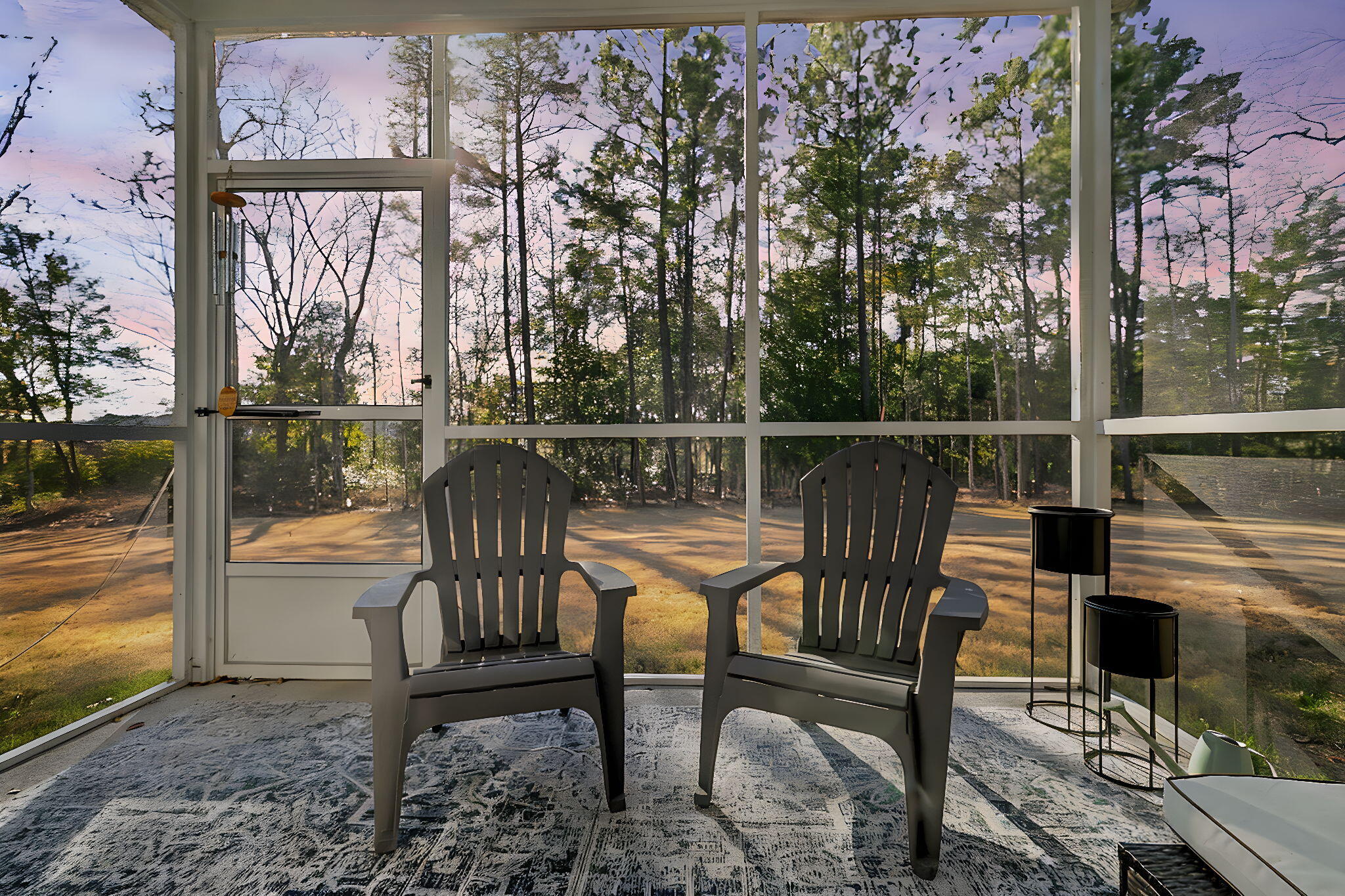 Furnished sunroom with two dark chairs and broad windows overlooking trees.