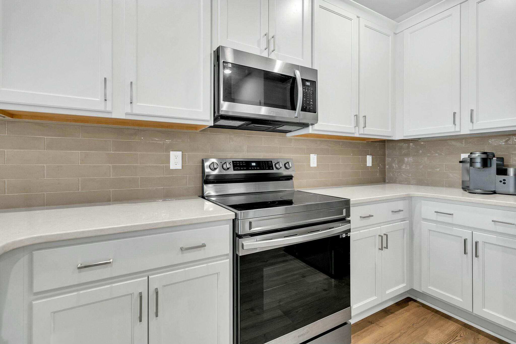 Kitchen with white cabinets, taupe tile backsplash, stainless steel appliances, and a Keurig coffee maker.