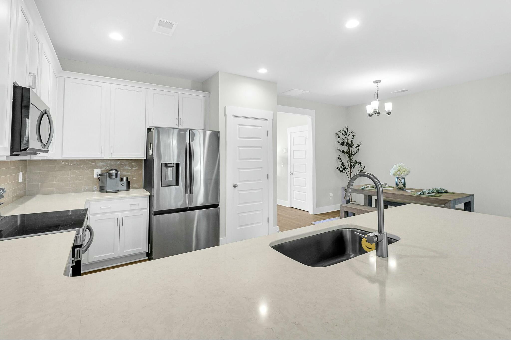 Bright kitchen with white cabinets, stainless appliances, and a large island with a sink.