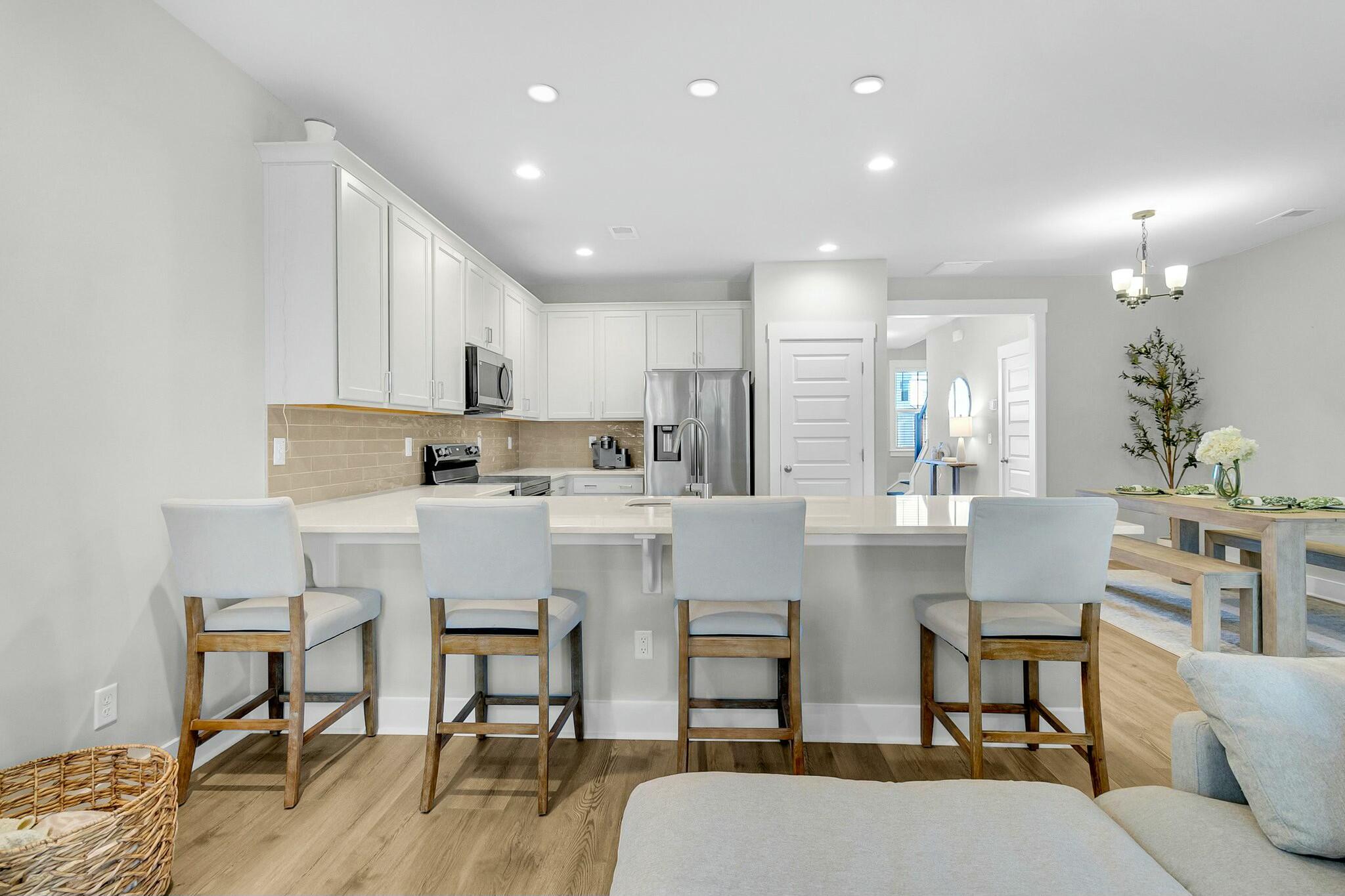 Open kitchen with white cabinets, stainless appliances, and a long island with four bar stools.