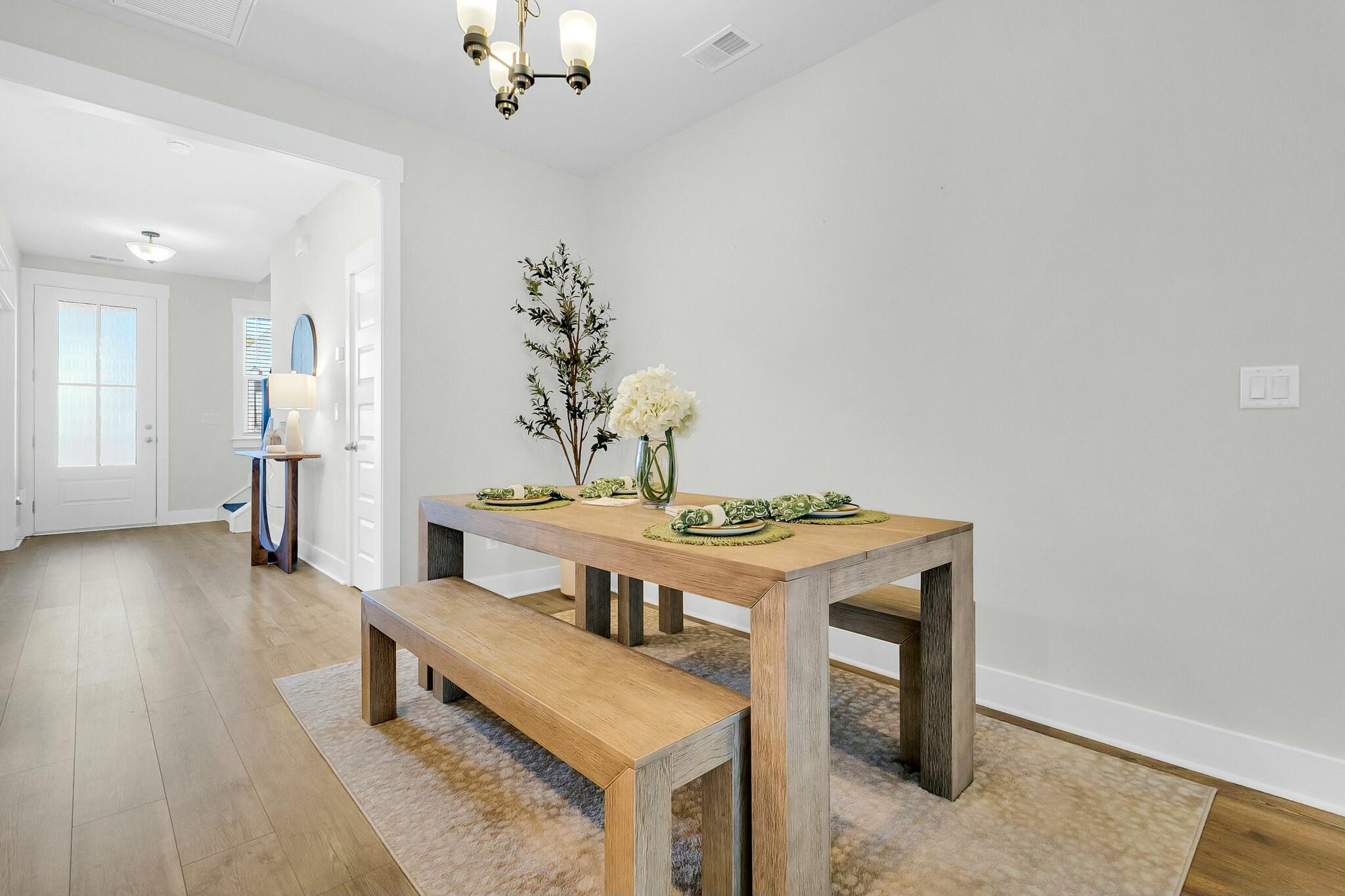 Staged dining room with a light wood table, bench, and green place settings near the entryway.