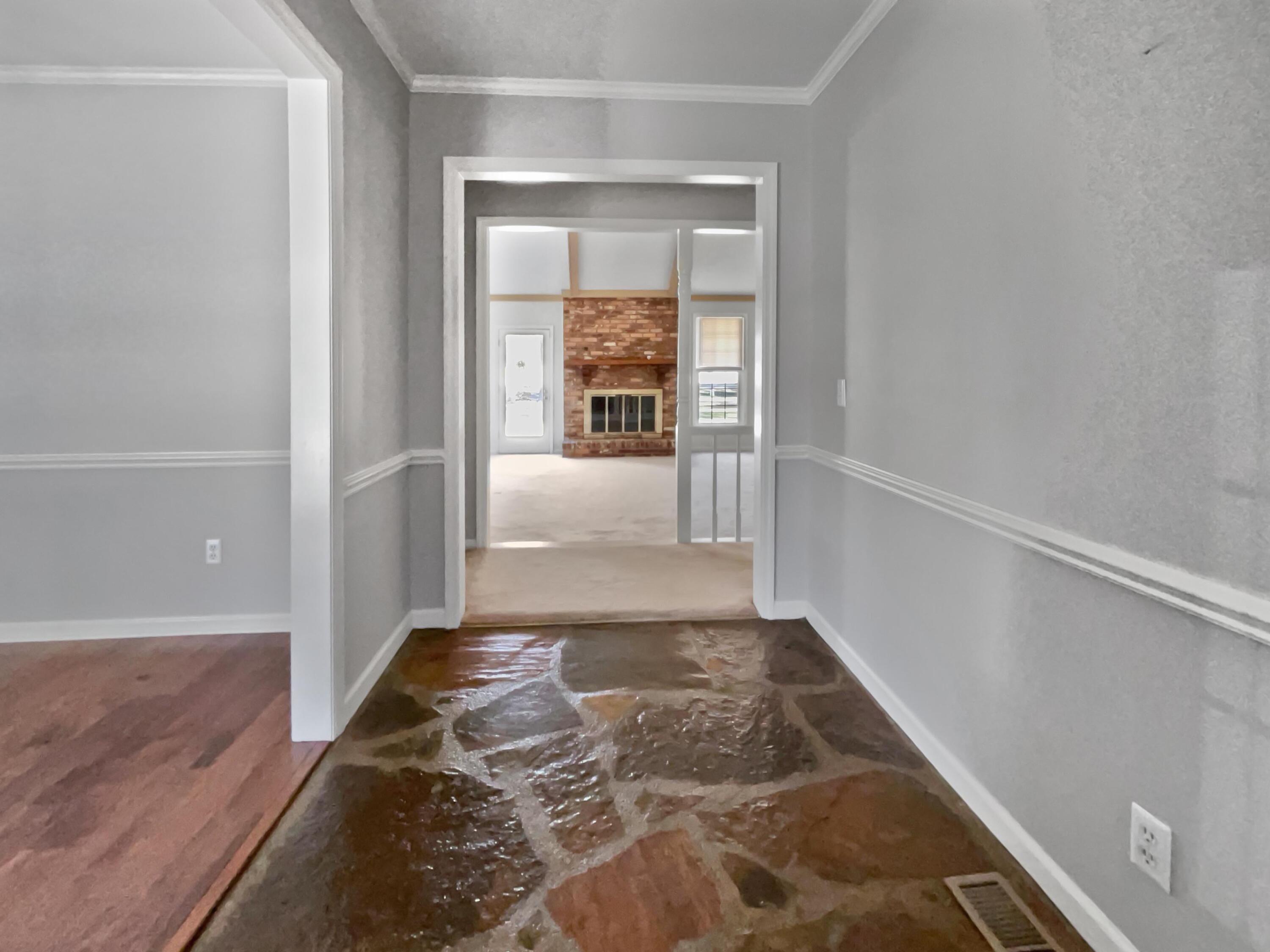Empty gray hallway with plastic-covered flooring leading to a living room with a brick fireplace.