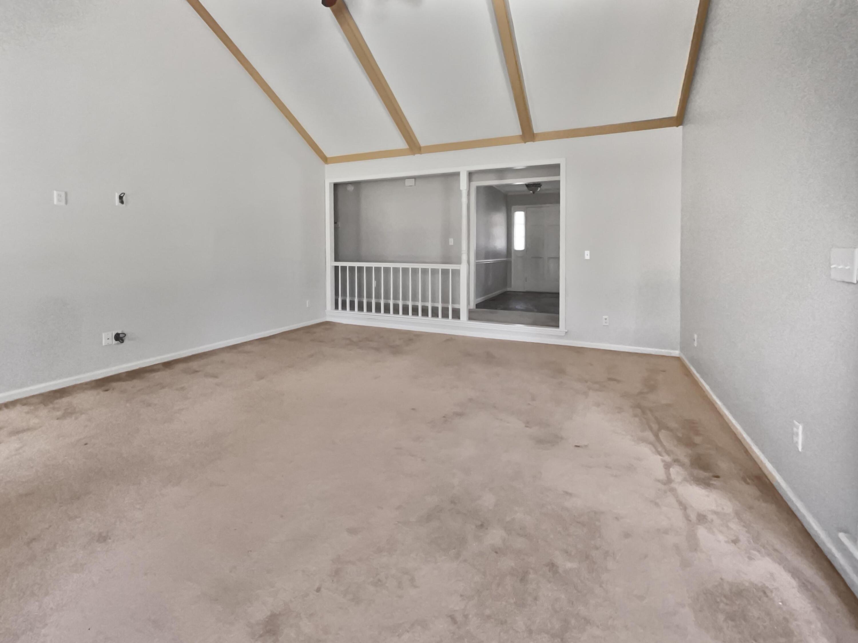 Empty carpeted room with a vaulted wood-beamed ceiling and a white-railed opening.