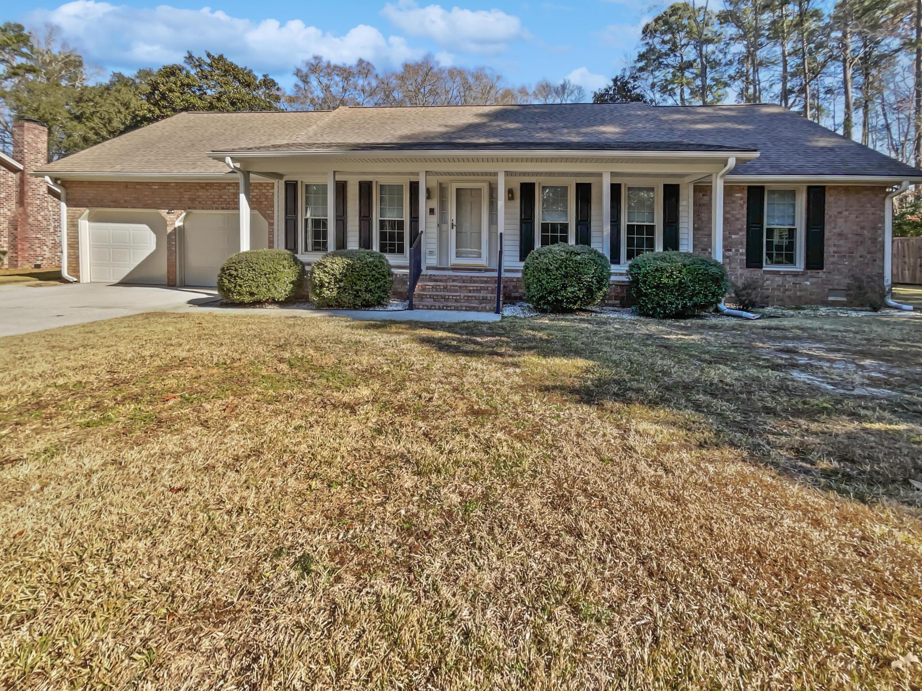 Single-story brick house with a covered porch, attached garage, black shutters, and dormant lawn.
