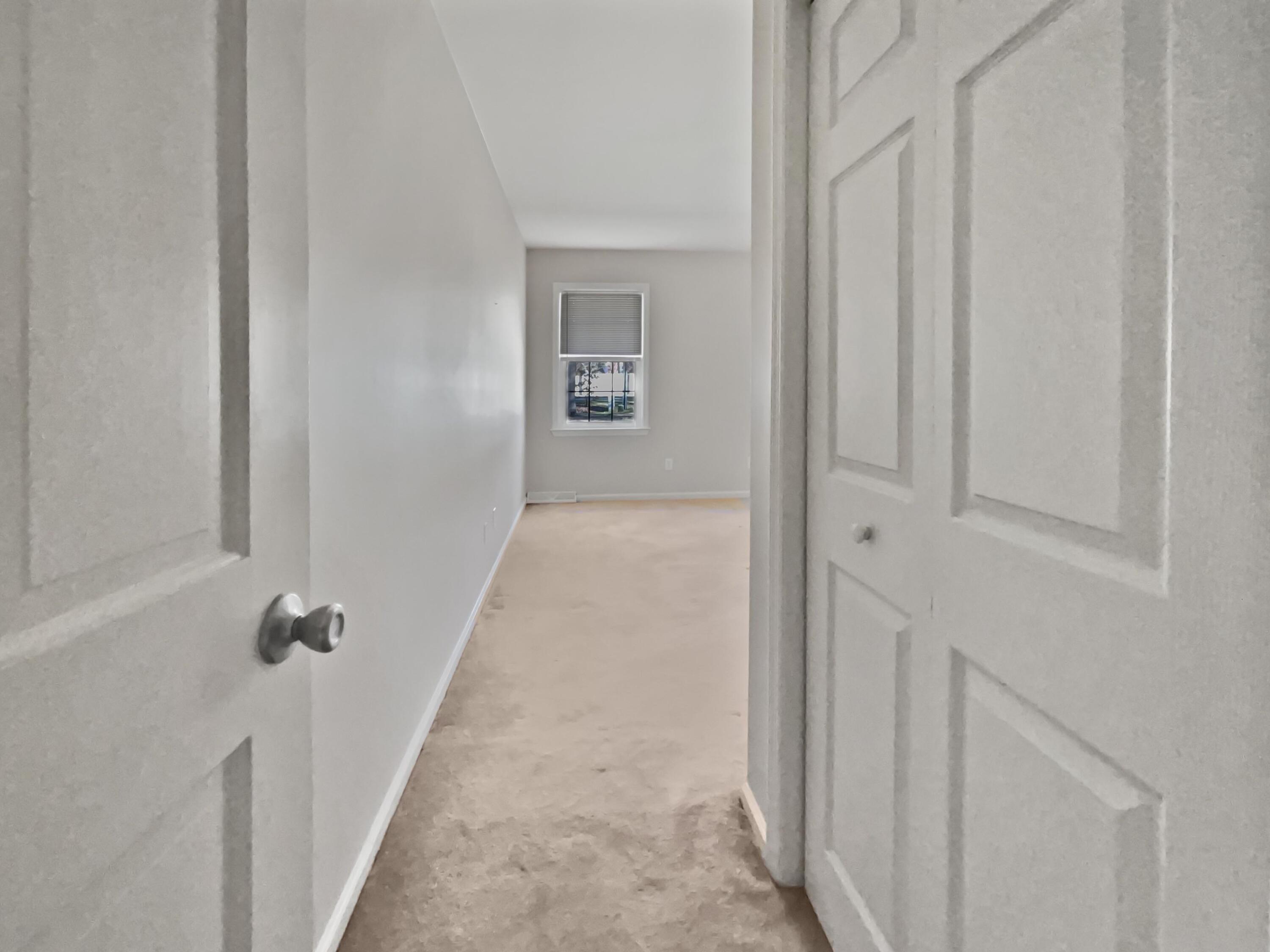 Empty carpeted room with gray walls and a window with a partially lowered blind.