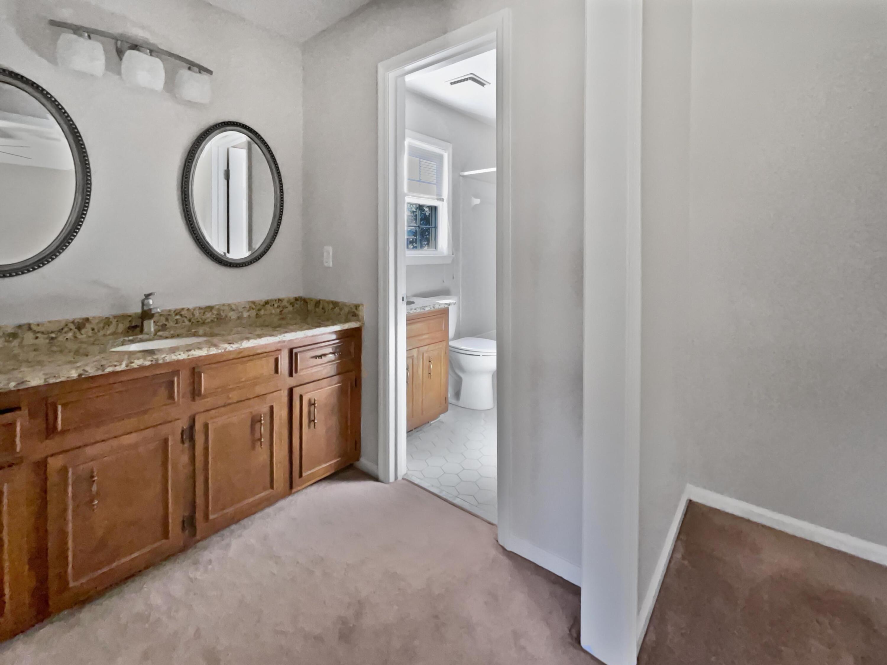 Bedroom vanity with wood cabinetry and granite counter beside an open bathroom doorway.