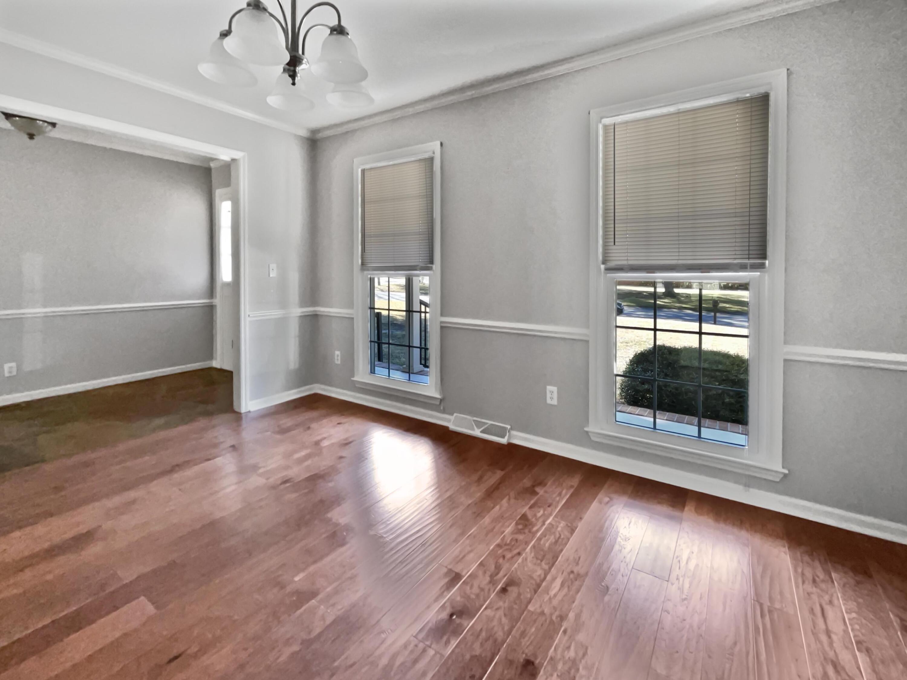 Empty room with hardwood floors, gray walls, and two tall windows with blinds.