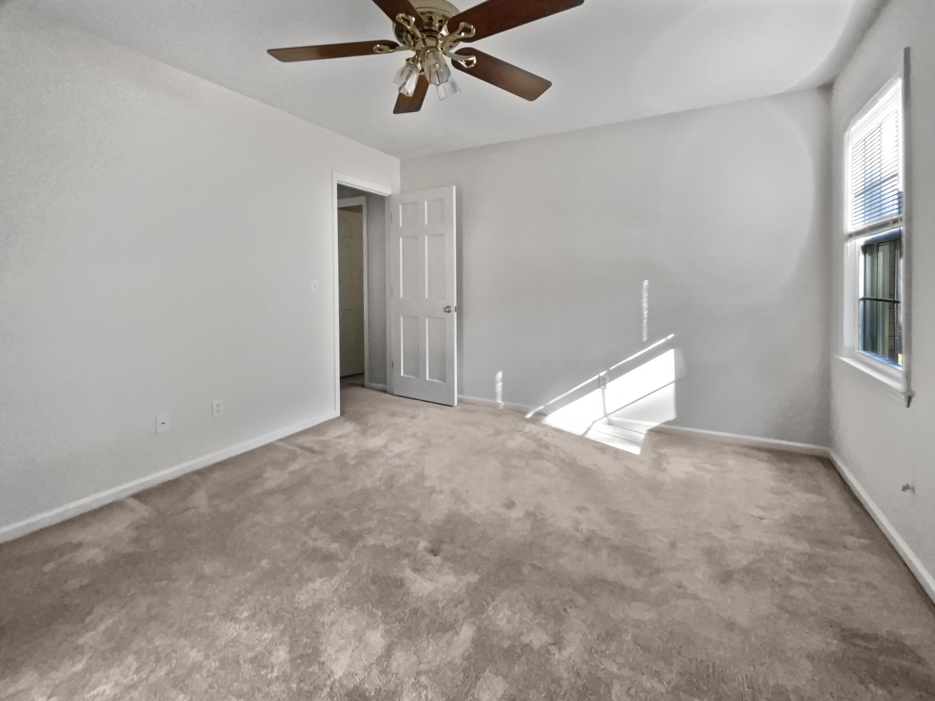 Empty carpeted room with a ceiling fan, window, and sunlight across the floor.