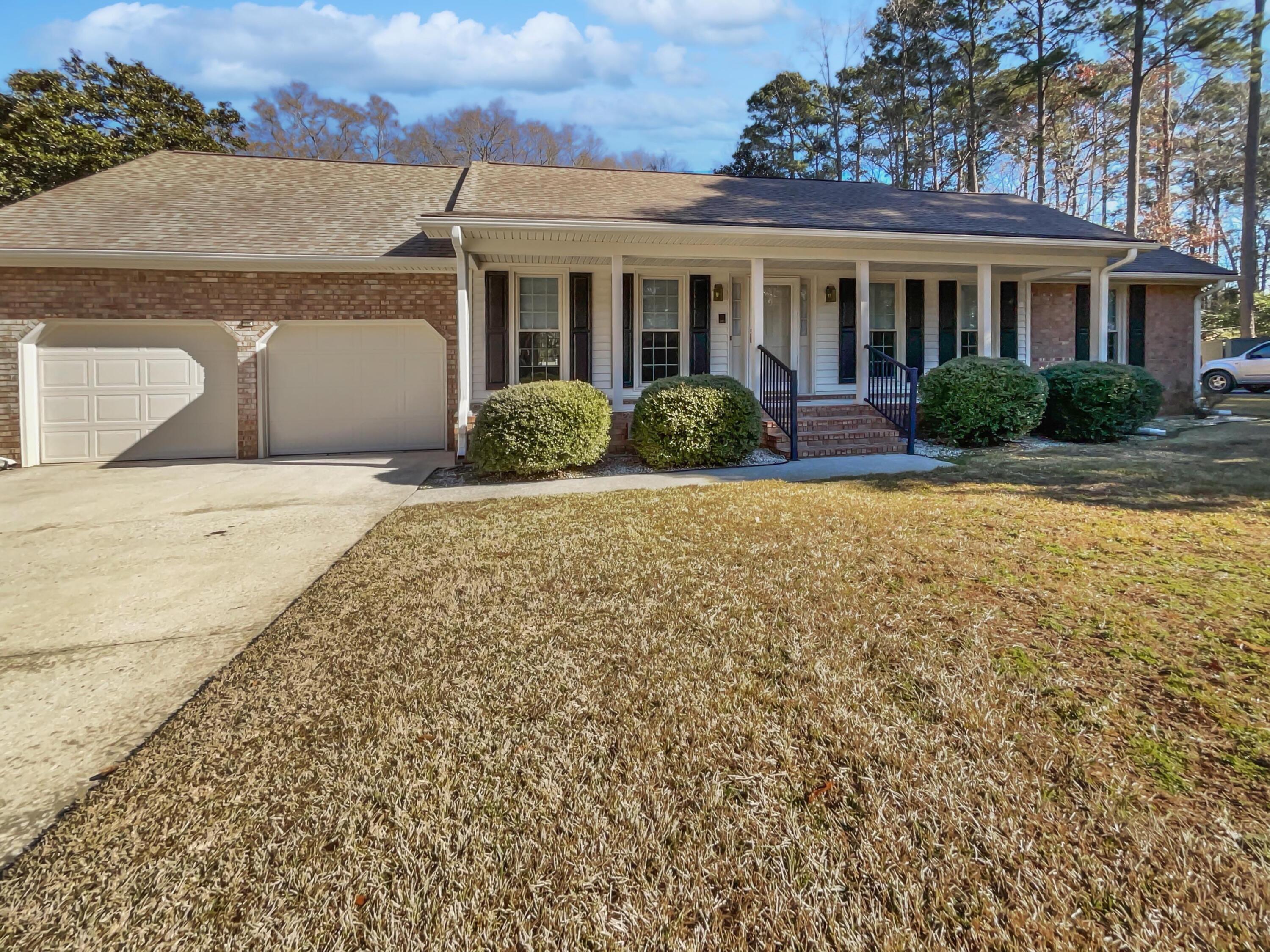 Single-story brick house with a long covered porch, dark shutters, and two garage doors.