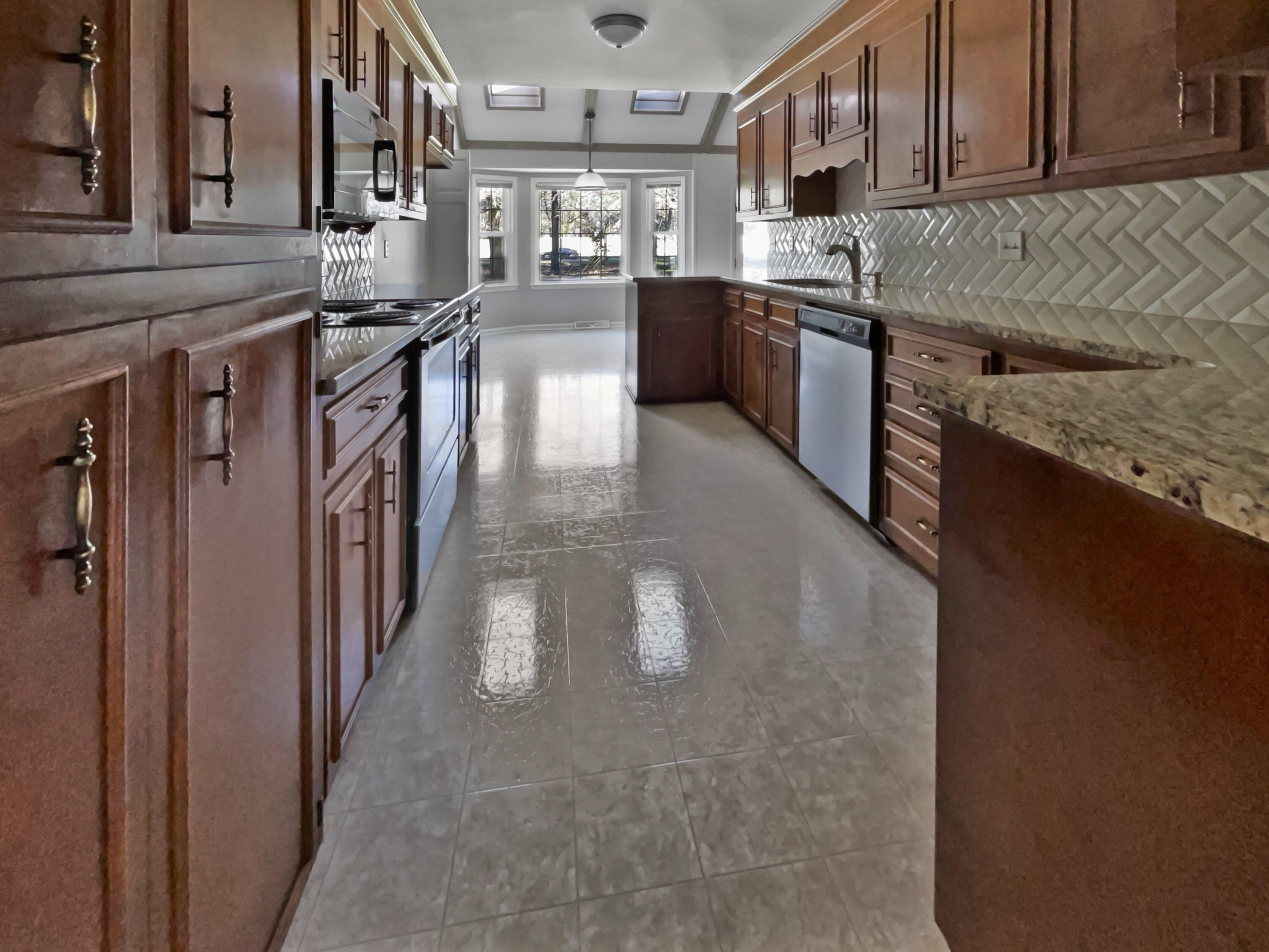Kitchen with dark wood cabinetry, granite counters, geometric tile backsplash, and a bright bay-window nook.