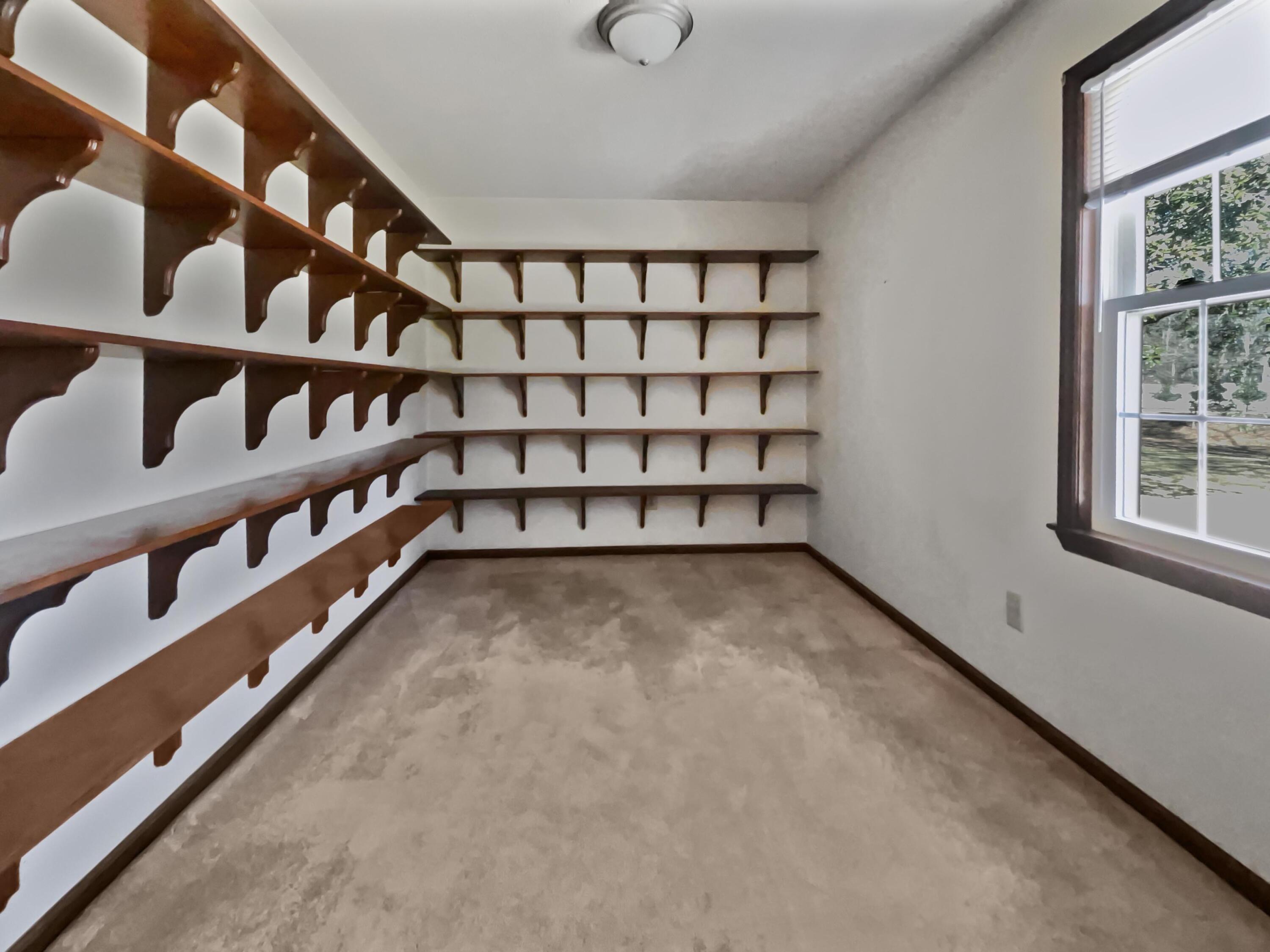 Walk-in closet with extensive dark wood shelving, beige carpet, and a window.