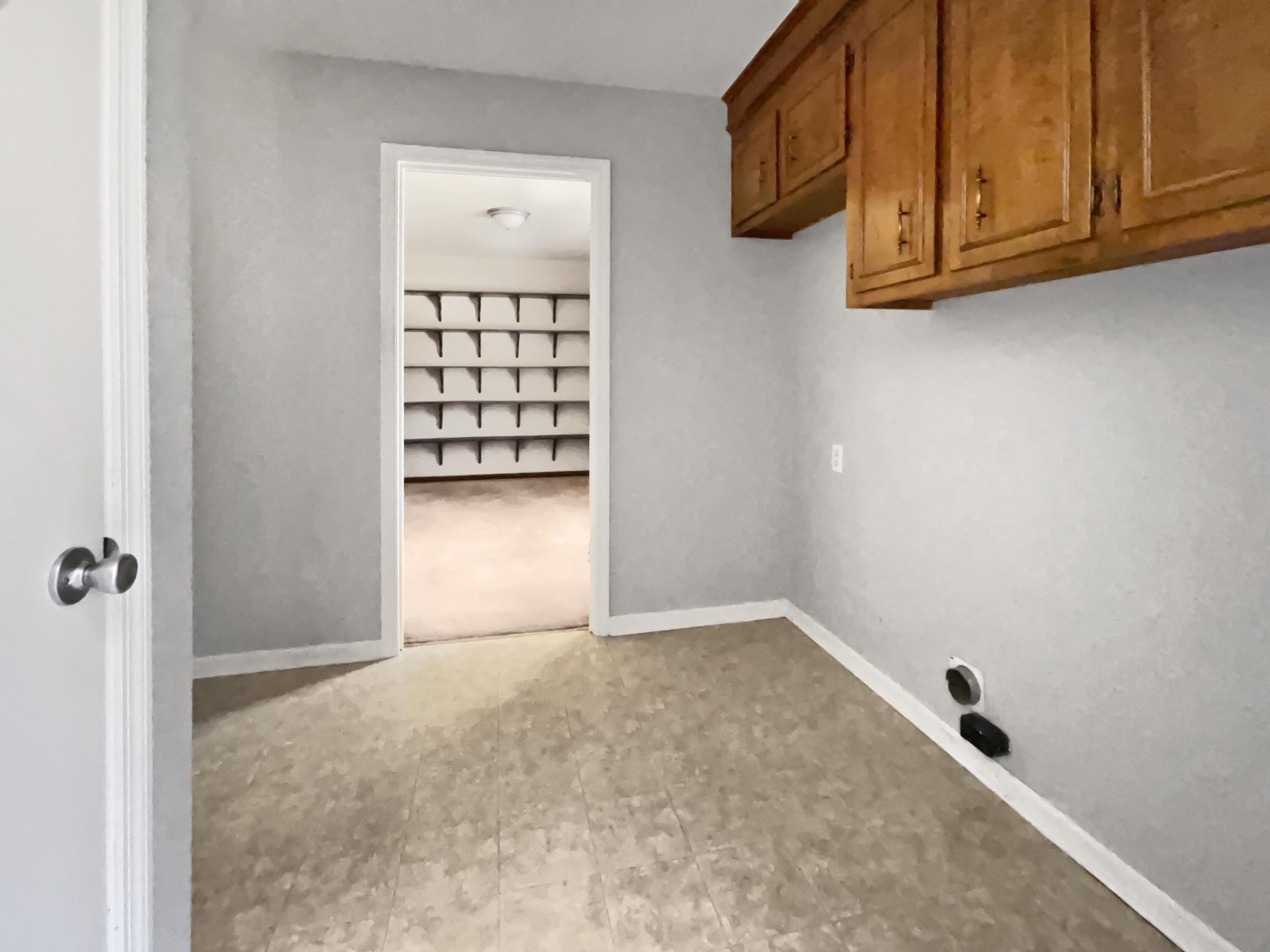 Empty utility room with wooden cabinets and a doorway to a carpeted room with wall shelves.