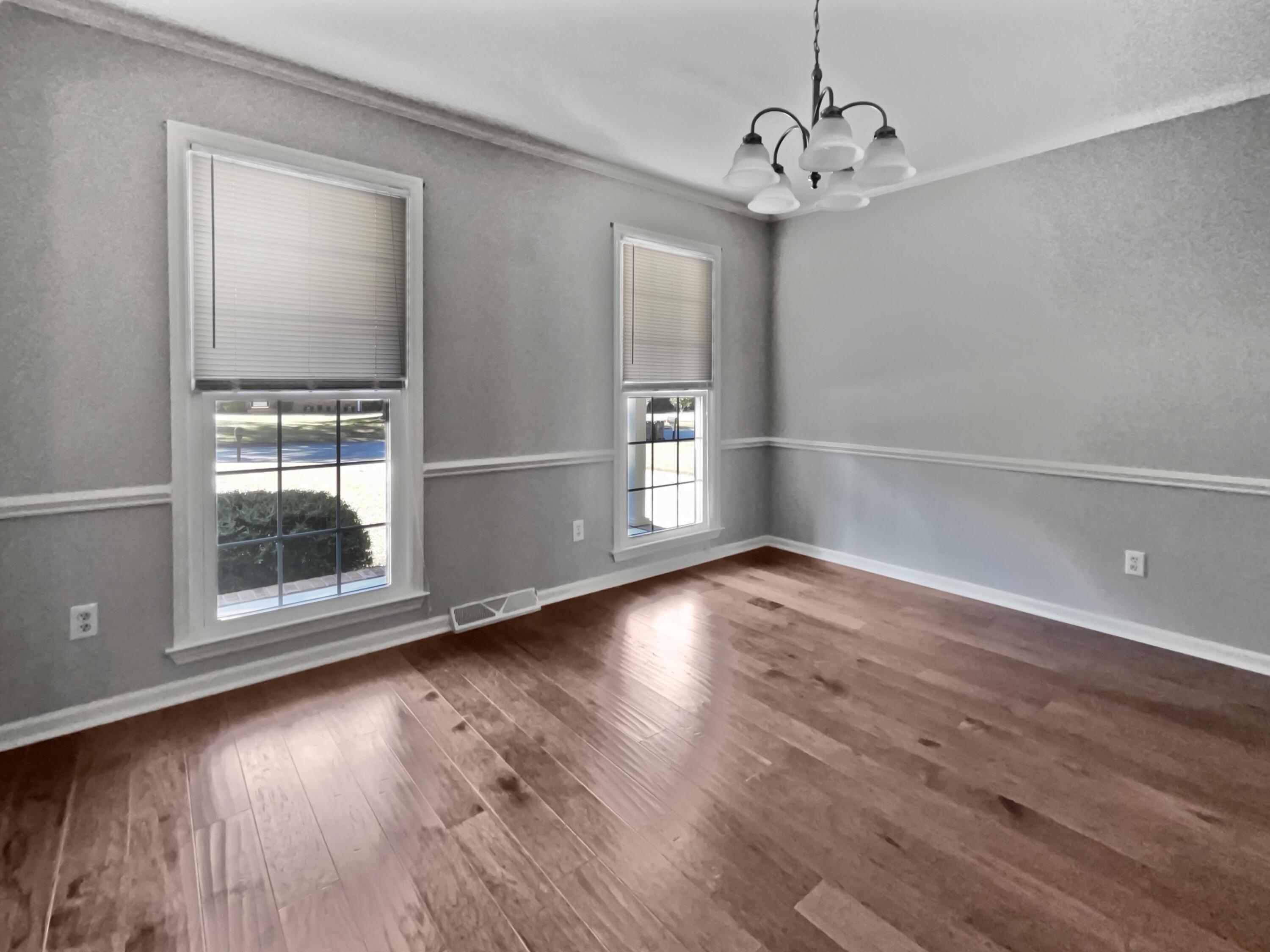 Empty dining room with hardwood floors, gray walls, two windows, and a chandelier.