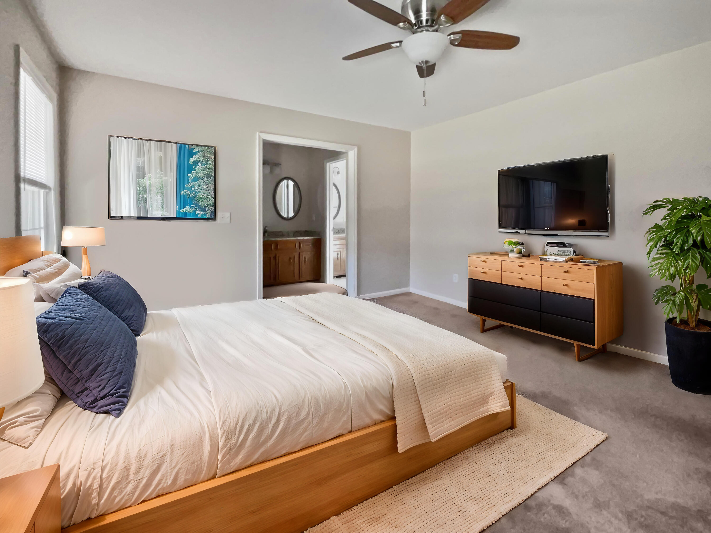 Furnished bedroom with white bedding, navy pillows, and an open doorway to the bathroom.