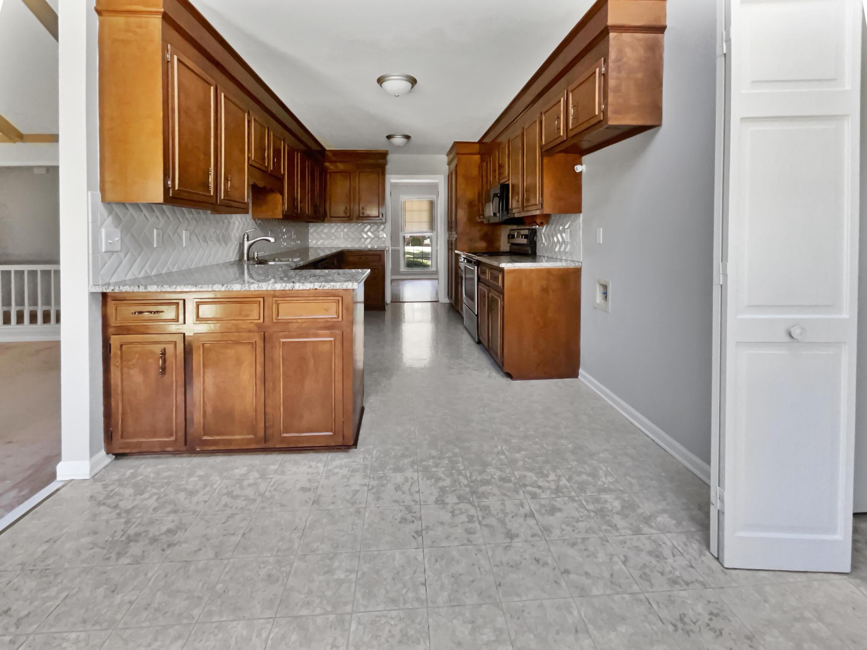 Kitchen with warm wood cabinets, patterned white backsplash, and gray tile floor.
