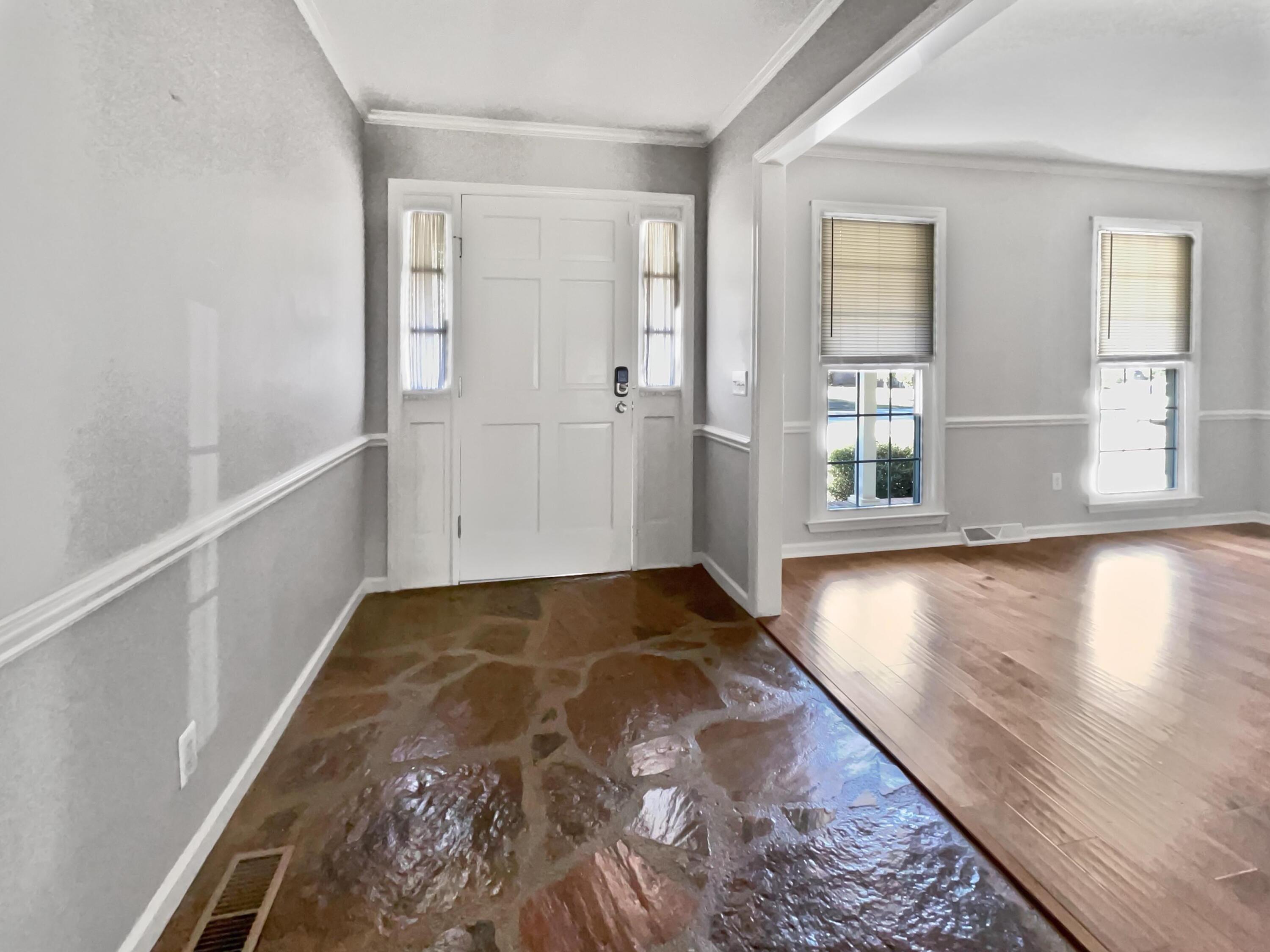 Entryway with a white front door, glossy stone-pattern floor, and adjoining hardwood-floored room.