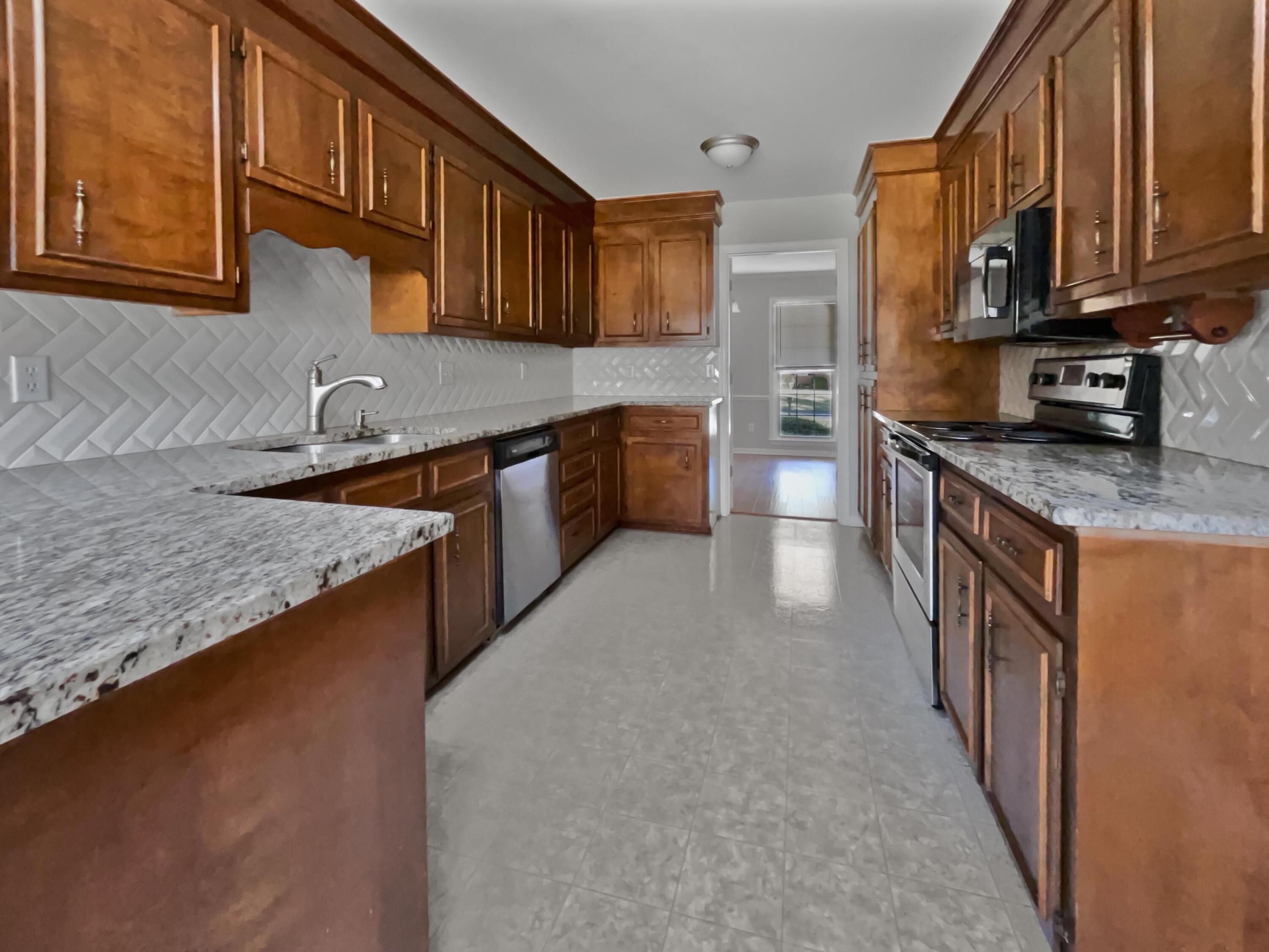 Galley kitchen with wood cabinets, speckled countertops, white herringbone backsplash, and stainless steel appliances.
