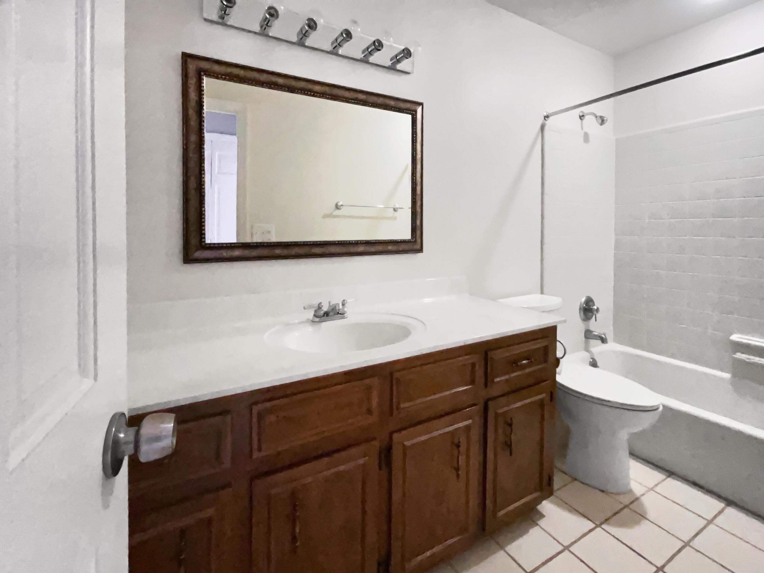 Bathroom with a dark wood vanity and framed mirror beside a toilet and tiled tub-shower.