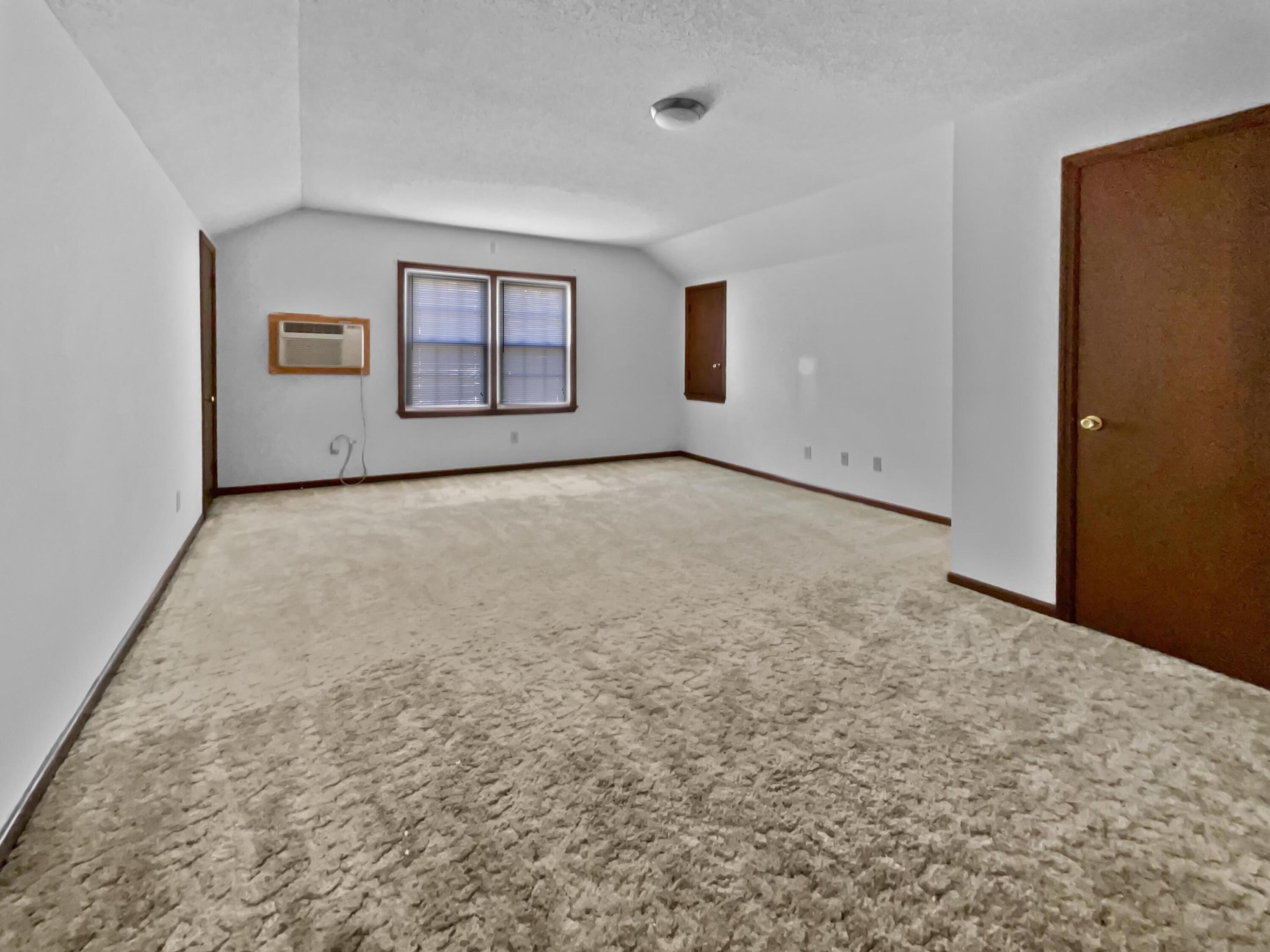 Empty carpeted bedroom with two windows, a window air conditioner, and dark wood trim.