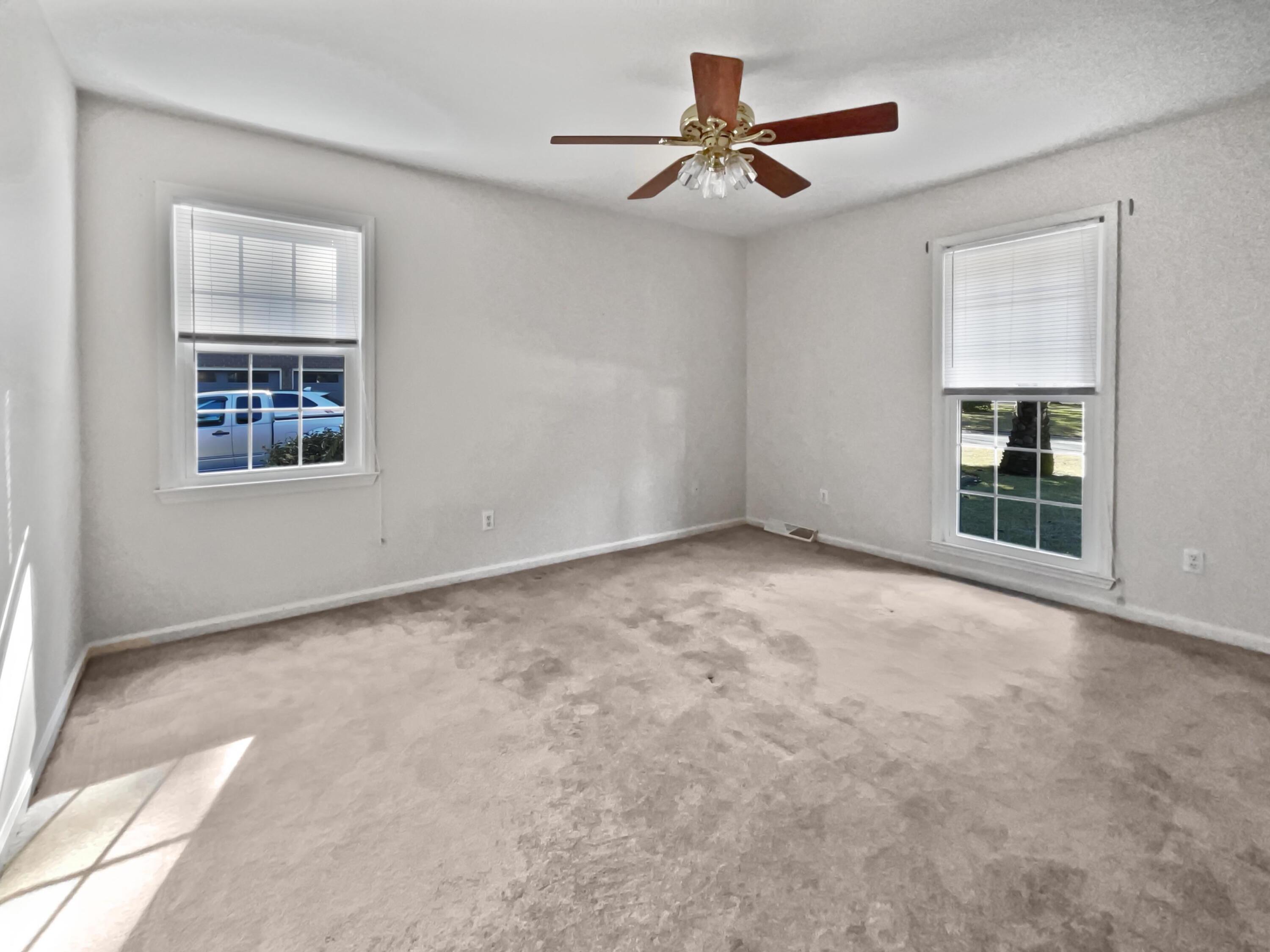 Empty bedroom with two windows, beige carpet, and a wood-blade ceiling fan.