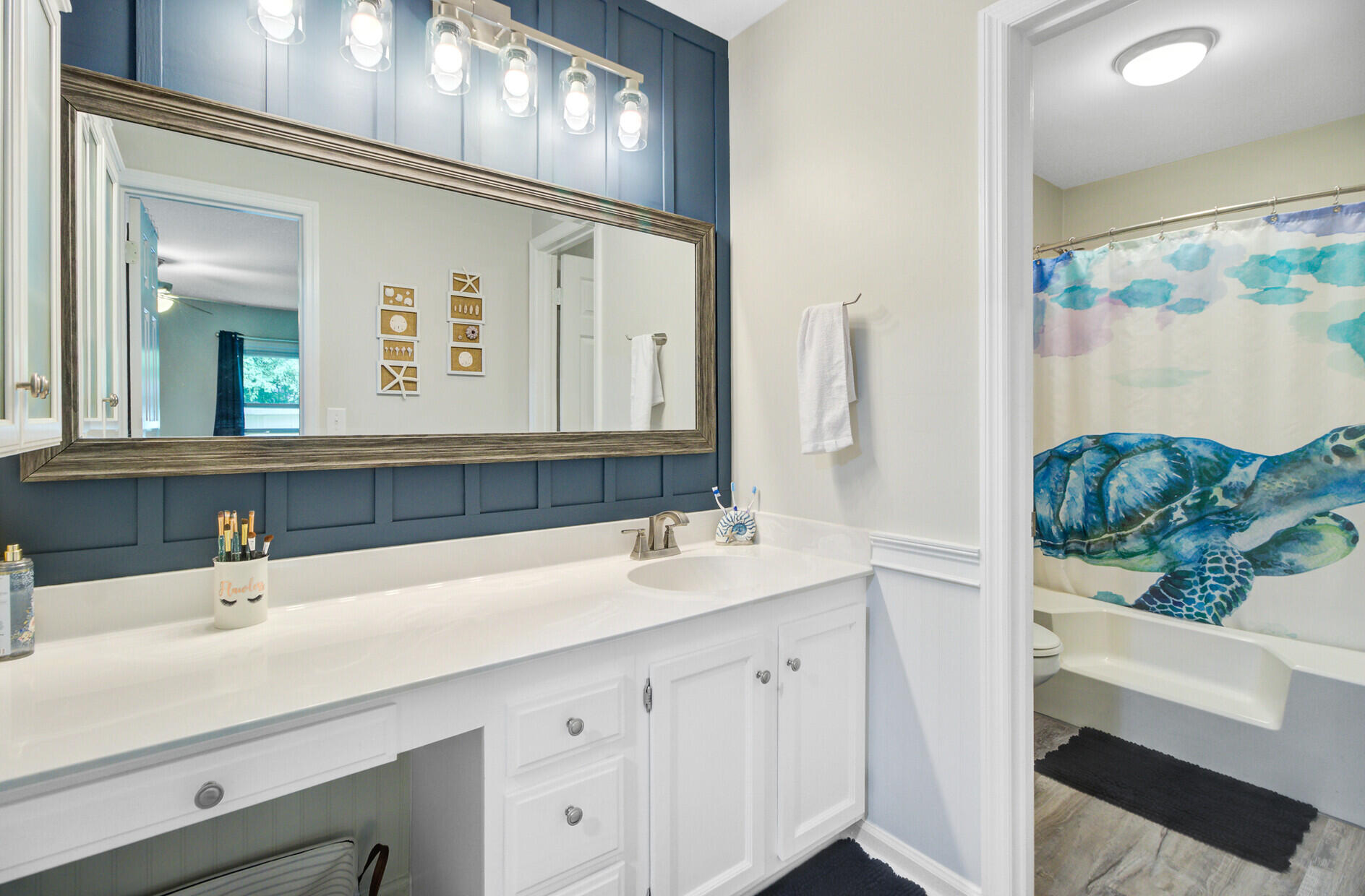 Bathroom with a white vanity, blue paneled accent wall, and sea-turtle shower curtain.