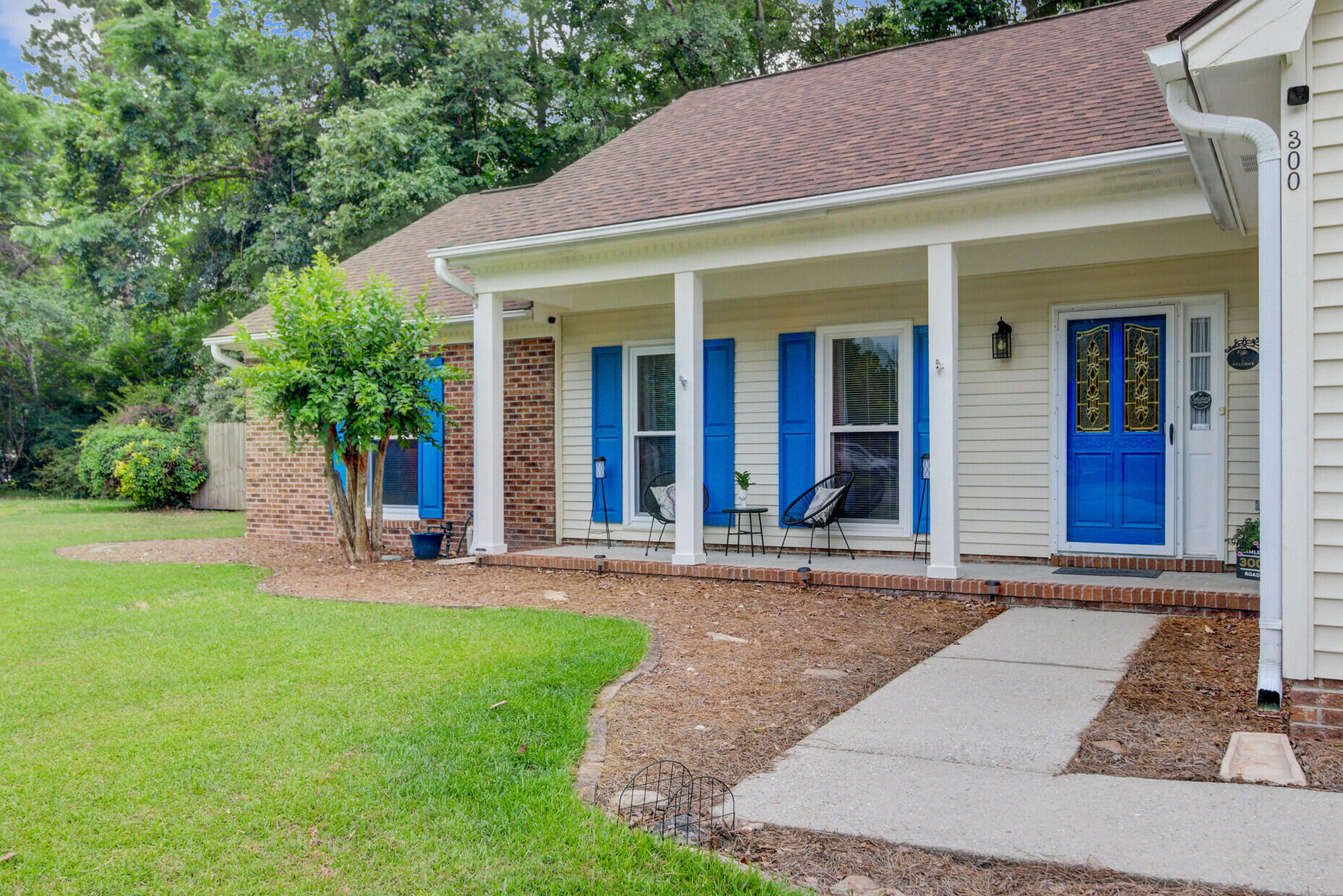 Home with a covered porch, bright blue shutters and door, and a walkway through the lawn.