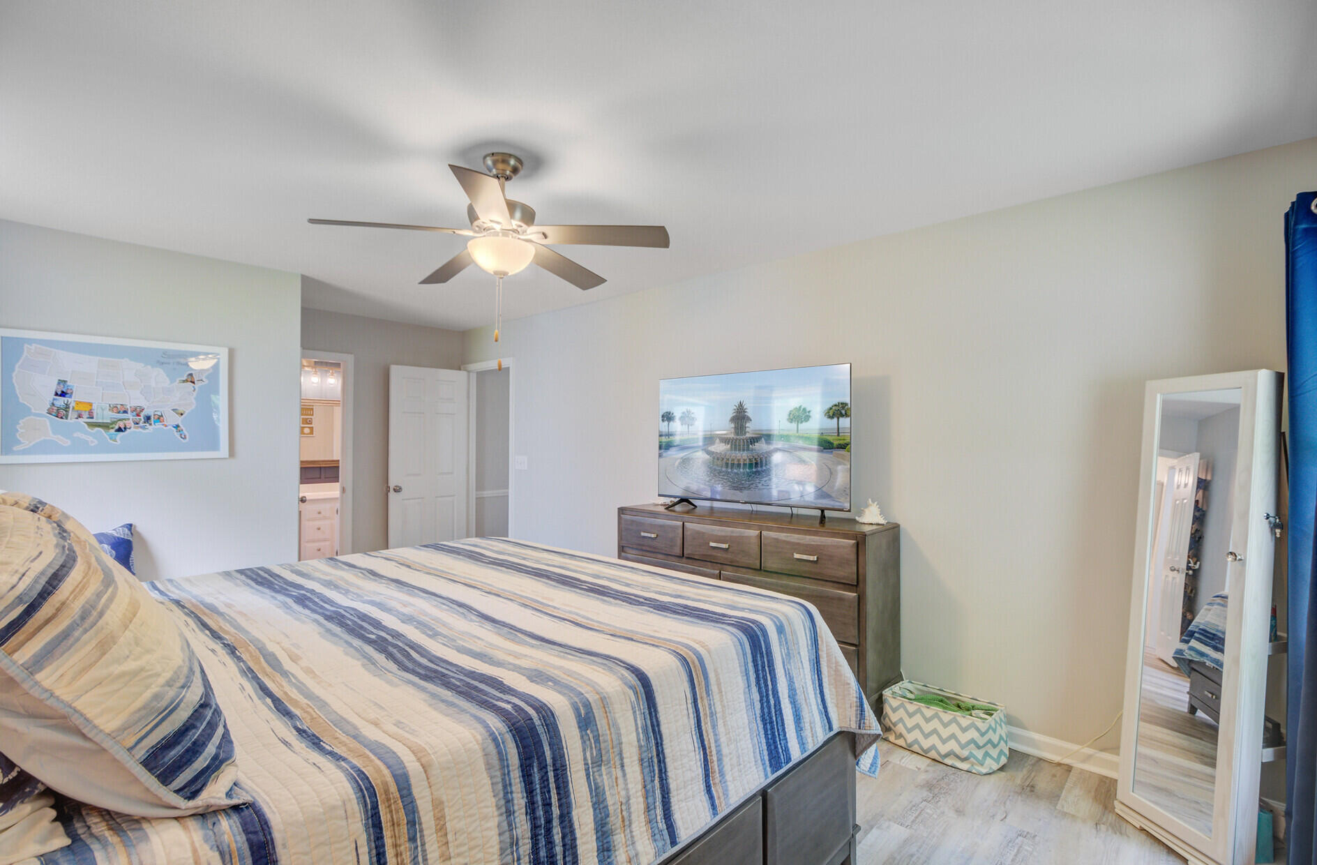 Bedroom with a blue-striped bedspread, ceiling fan, dresser, television, and full-length mirror.