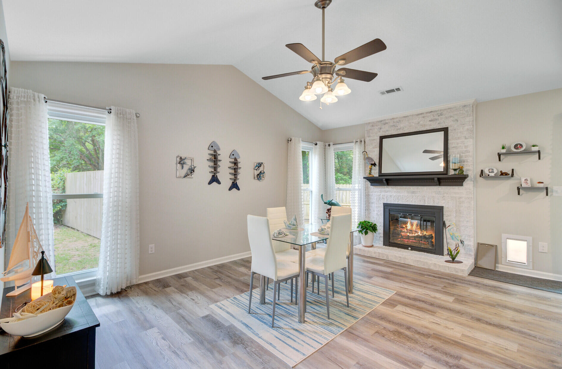 Living and dining area with a vaulted ceiling, stone fireplace, glass dining table, and curtained windows.