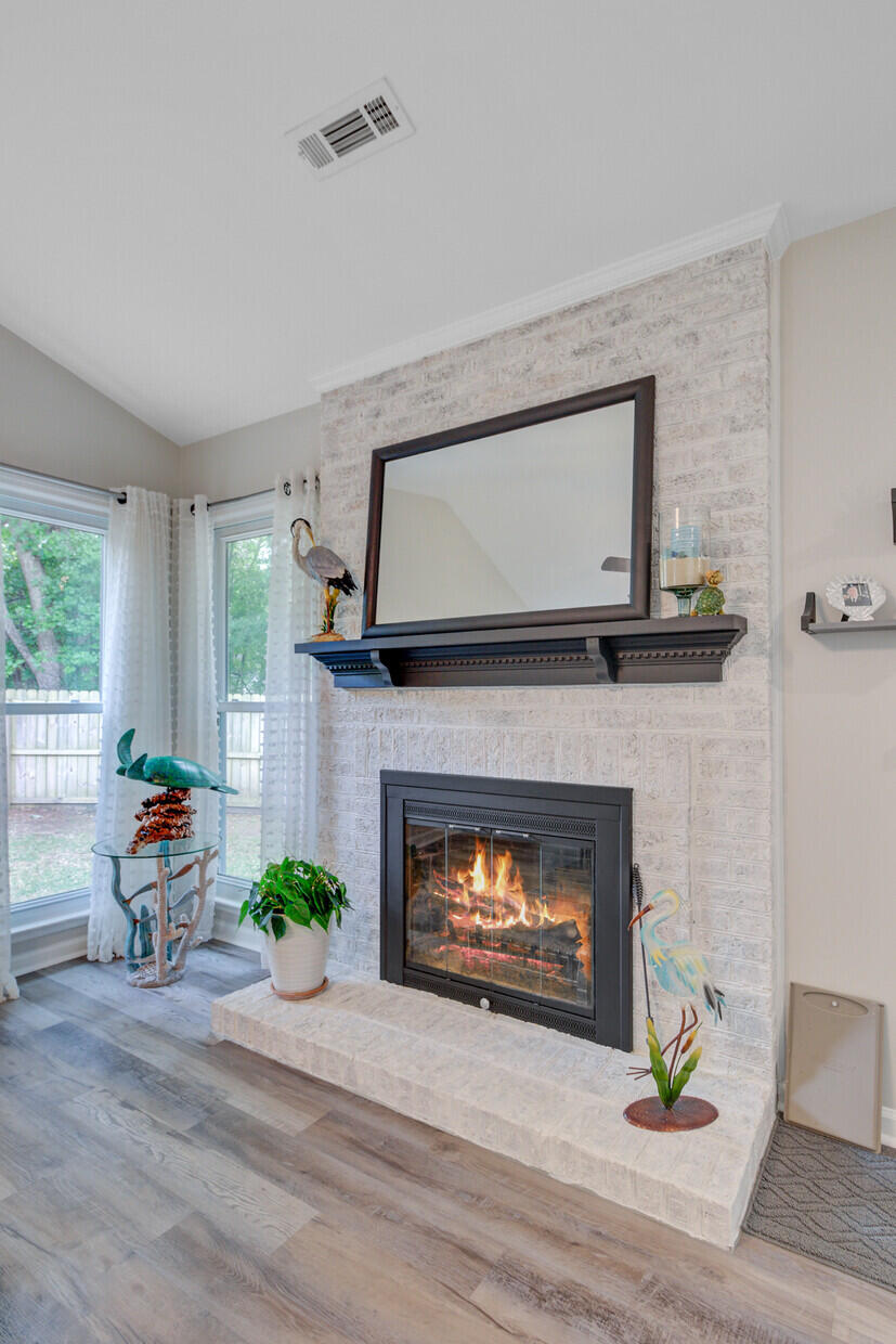 Living room fireplace with a lit fire, whitewashed brick surround, dark mantel, and large mirror.